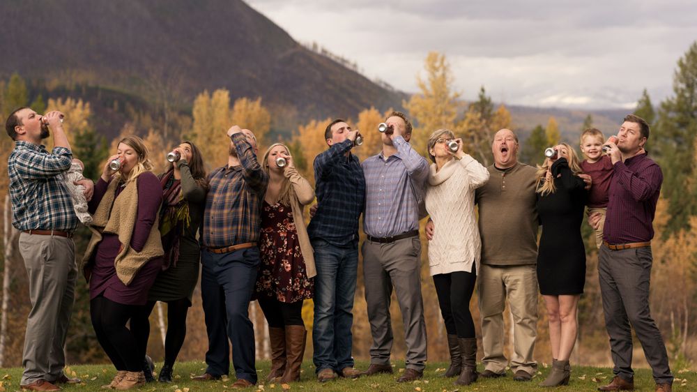 Large group poses together for a casual outdoor photo with mountains and fall foliage in the background.