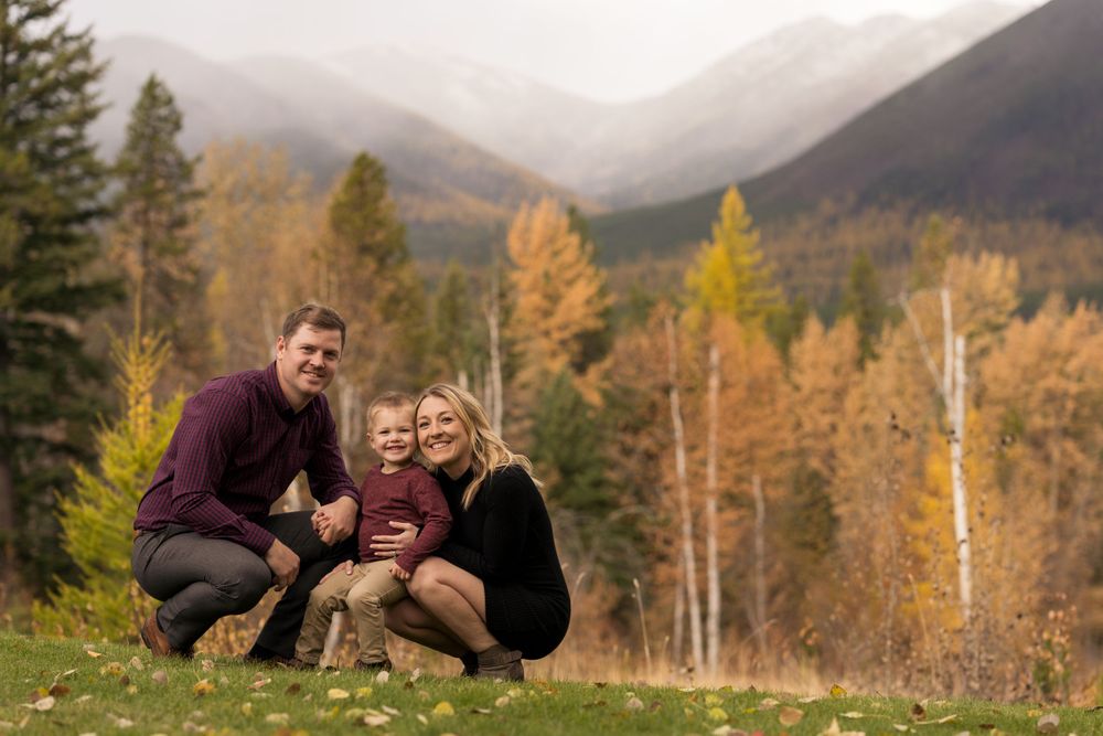 A young family shares a tender moment against a scenic mountain landscape with fall colors.