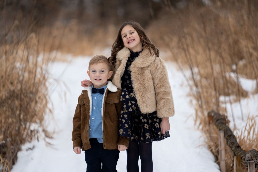 Two children standing together on a snowy path wearing winter coats.