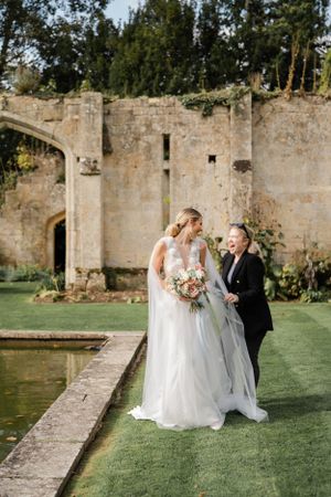 A couple poses by ancient stone ruins near a reflective pond during their wedding.