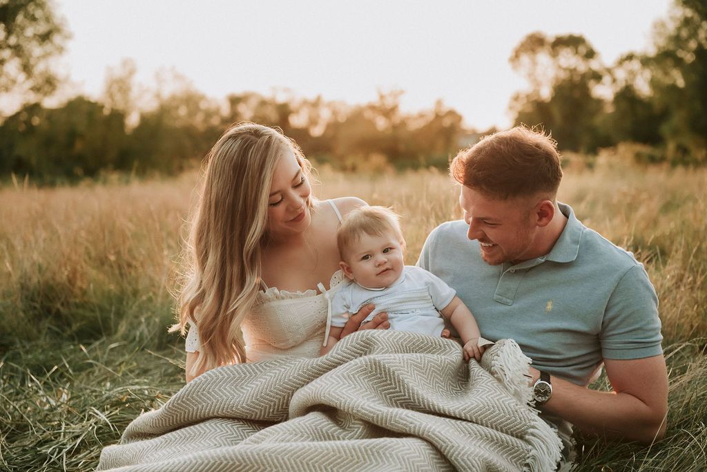 Family relaxing on blanket in grassy field during golden hour sunset.