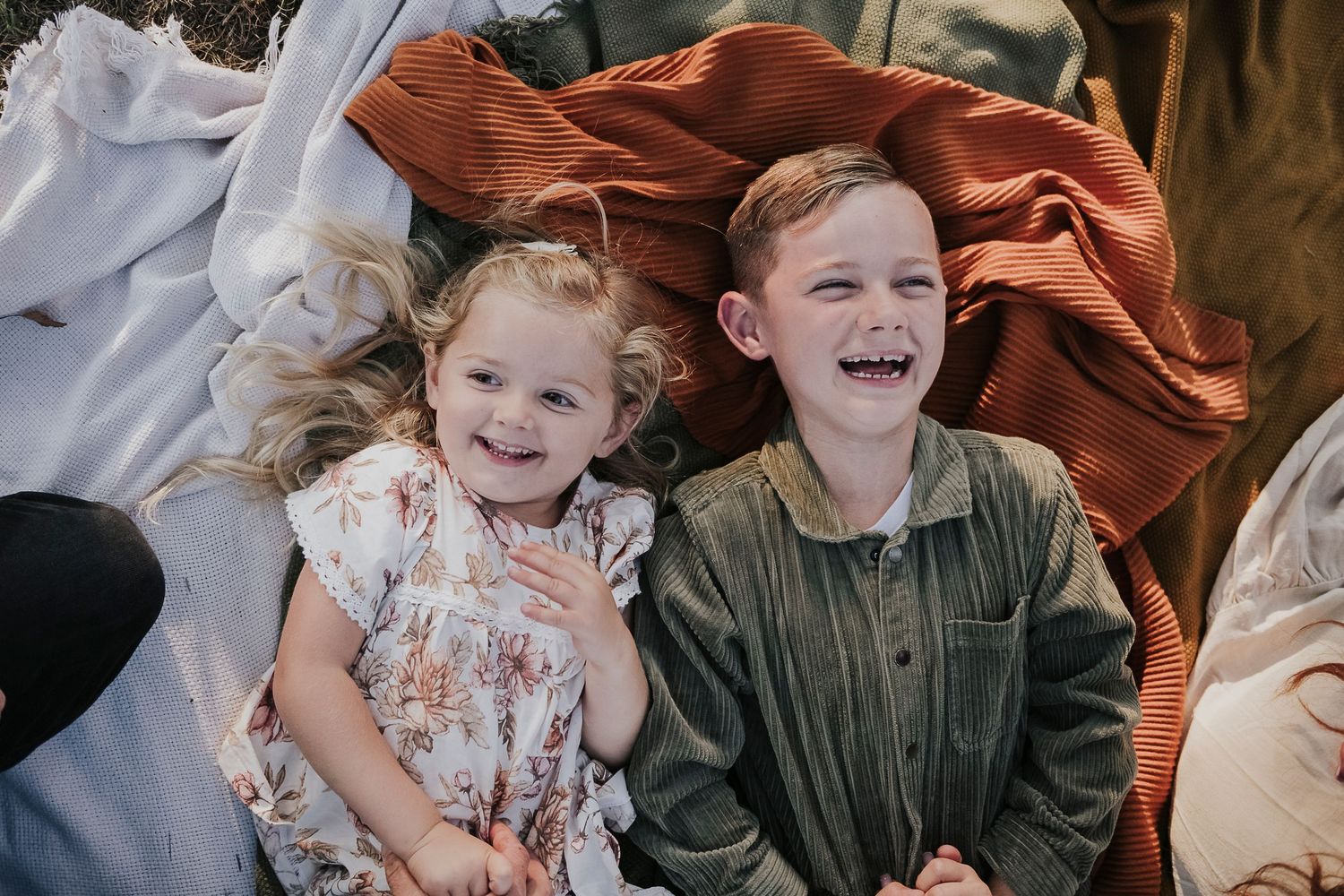 Candid family moment captured on blankets with rust-colored backdrop.