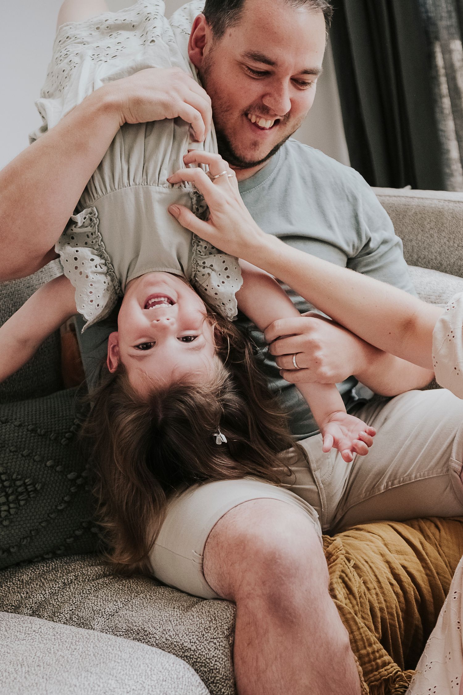 Playful family moment captured on grey couch during indoor photoshoot.