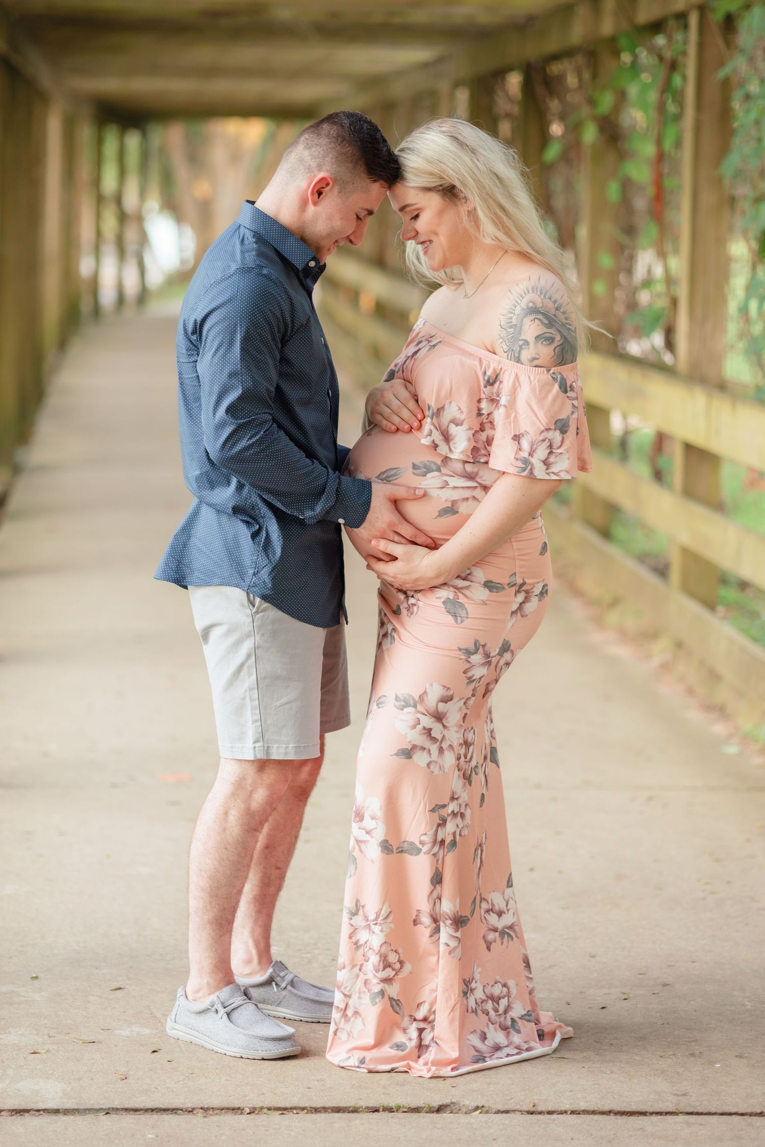 A couple in casual attire embraces while expecting on a wooden bridge pathway.