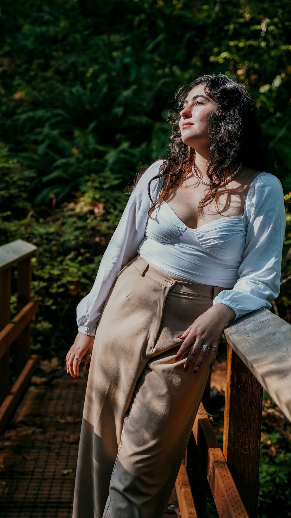 Person in white crop top and beige pants posing on wooden deck in forest setting.