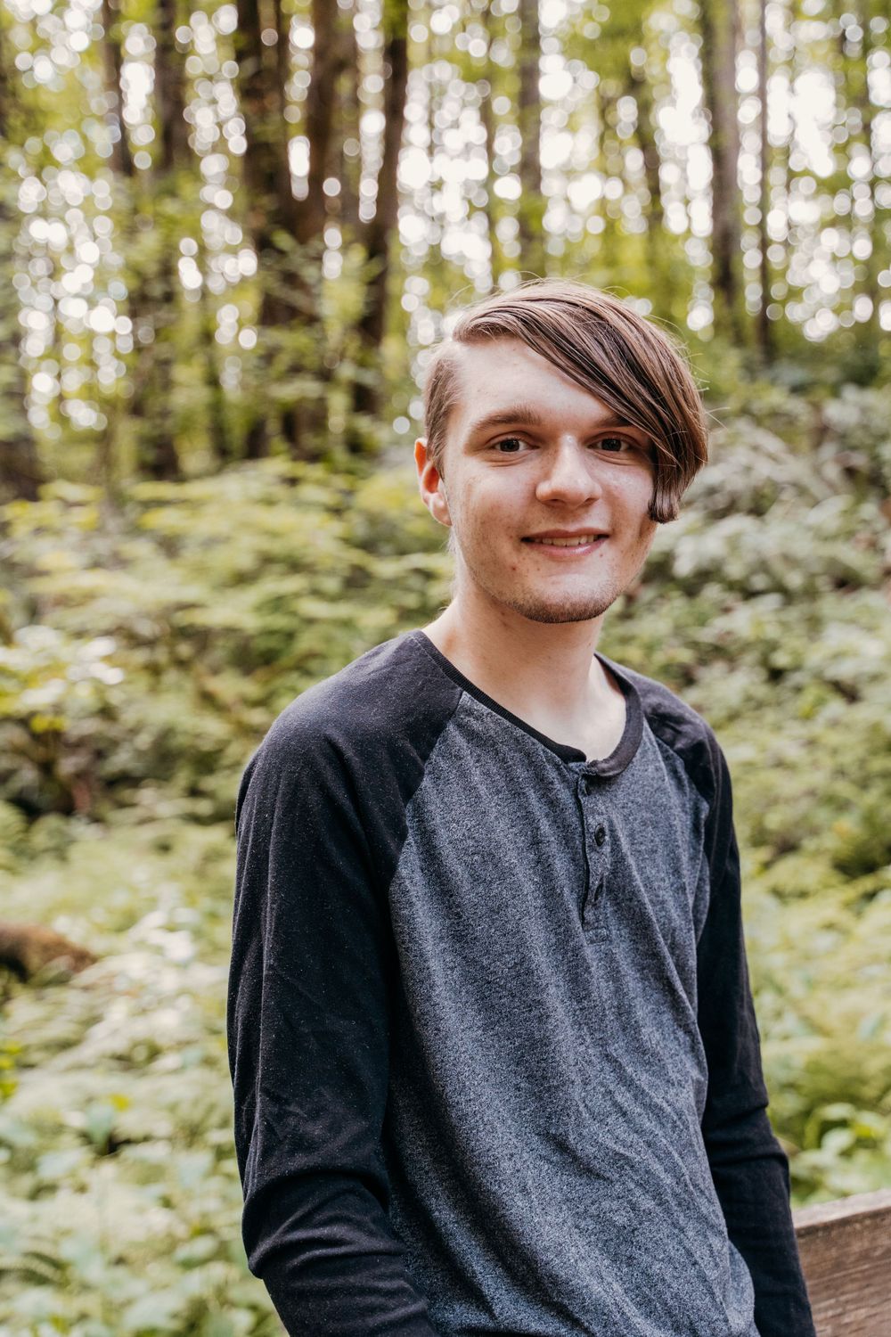 Portrait of someone in a grey henley shirt standing in a lush green forest setting.
