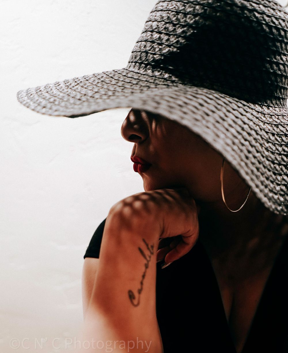 Artistic portrait of someone wearing a wide-brimmed straw hat against light background.