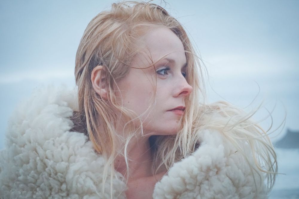 Ethereal winter portrait with blonde hair and fur coat against misty background.