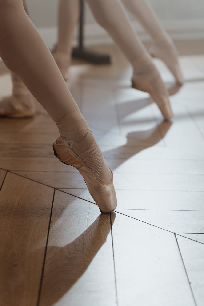 Ballet dancers feet in pointe shoes practicing on wooden floor.