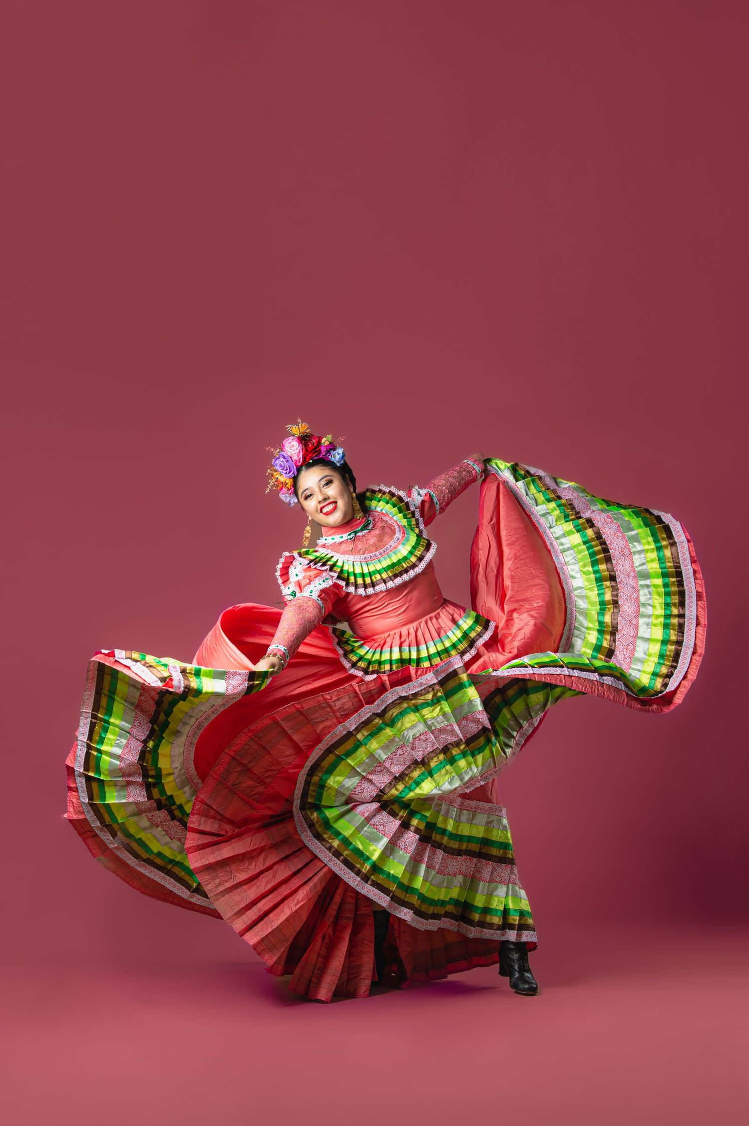 Dancer performs in vibrant red and green traditional Mexican folkloric dress with flowing ruffled skirt.