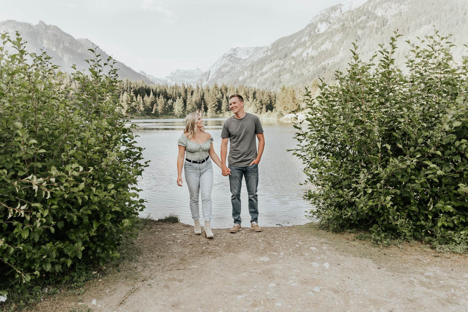 Three people walking on path with mountain lake and forest landscape.