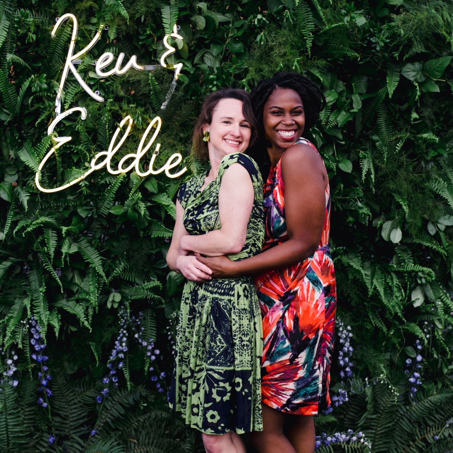 Two friends embracing against a lush green garden wall with text overlay.