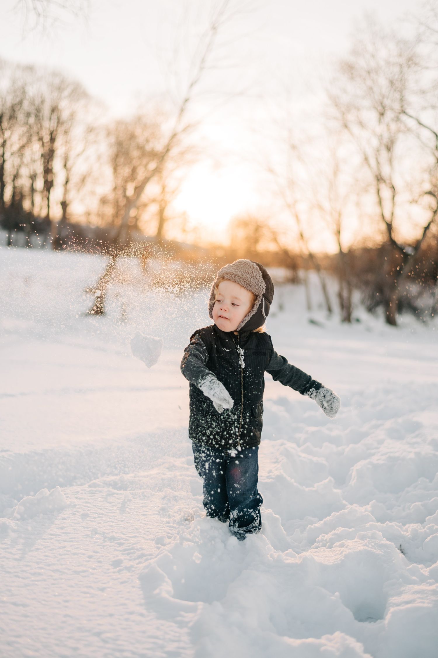 photo of a little boy throwing a snowball at sunset on a snowy beach