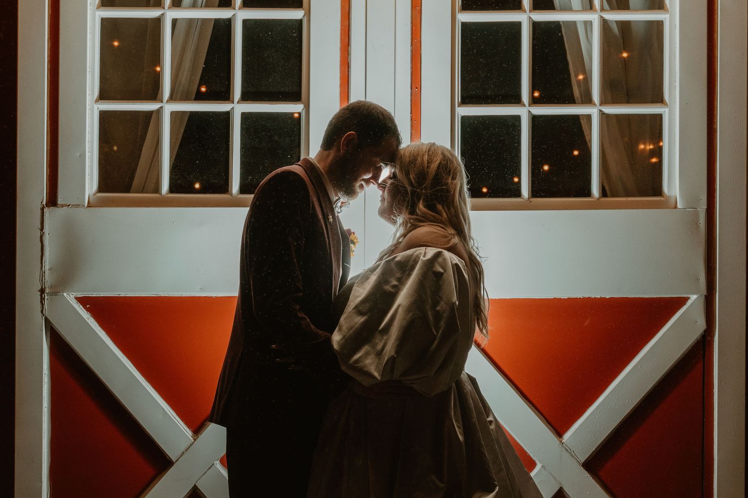 Romantic couple embrace near rustic barn door at dusk.