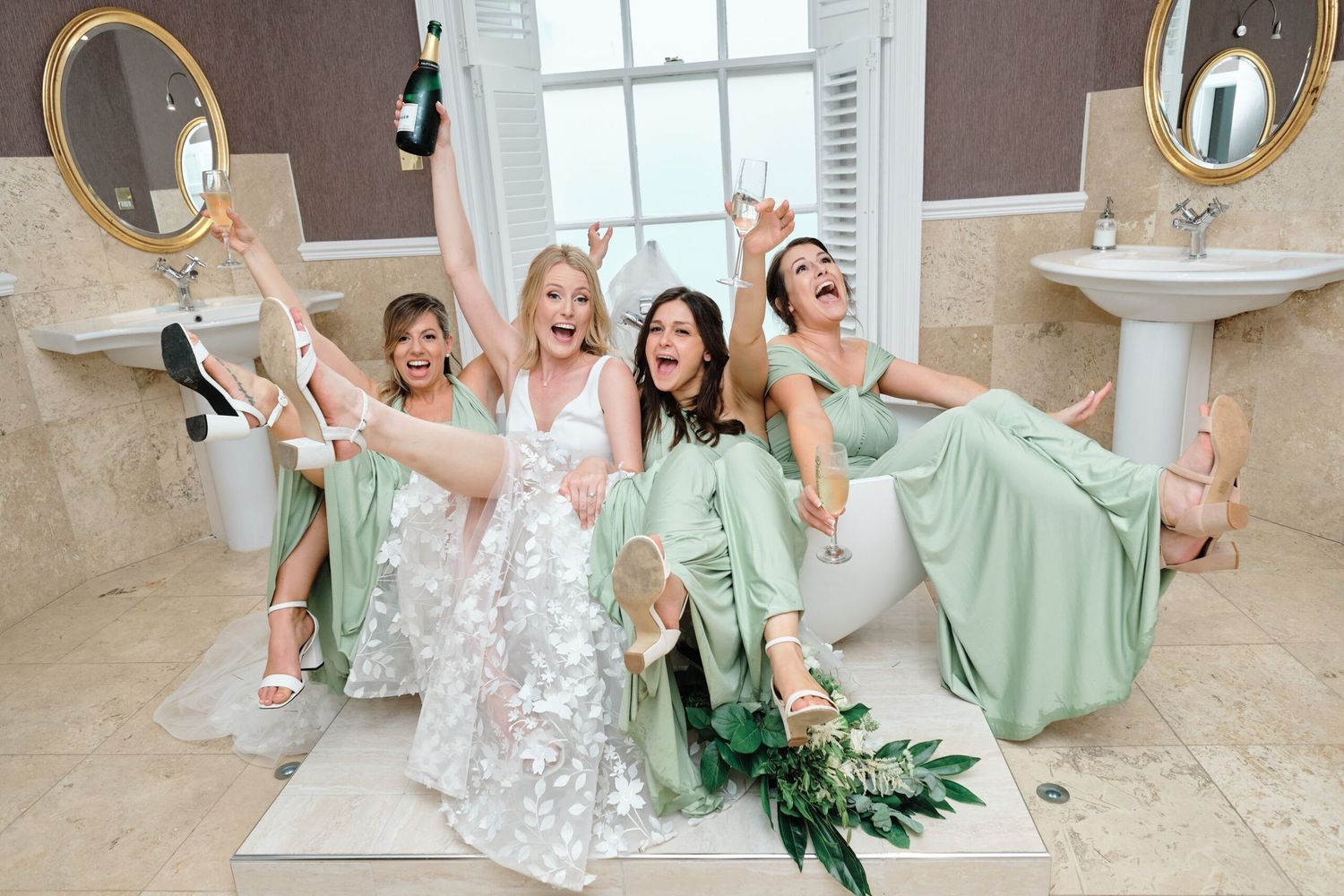 Bridal party in mint green dresses celebrates joyfully in elegant bathroom setting.