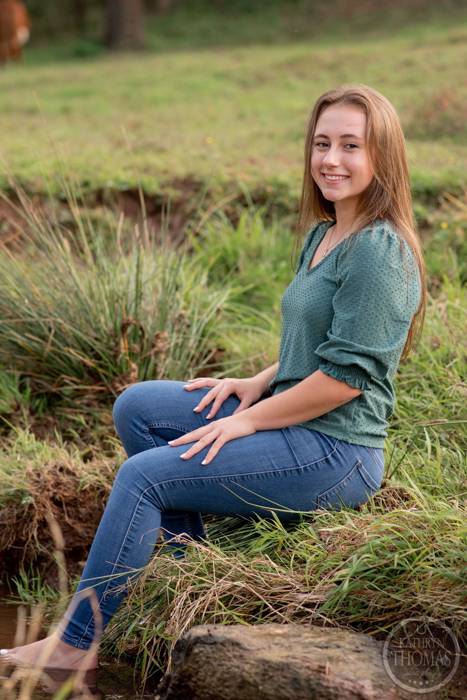 A person in green blouse and jeans sits on a log in a natural outdoor setting.