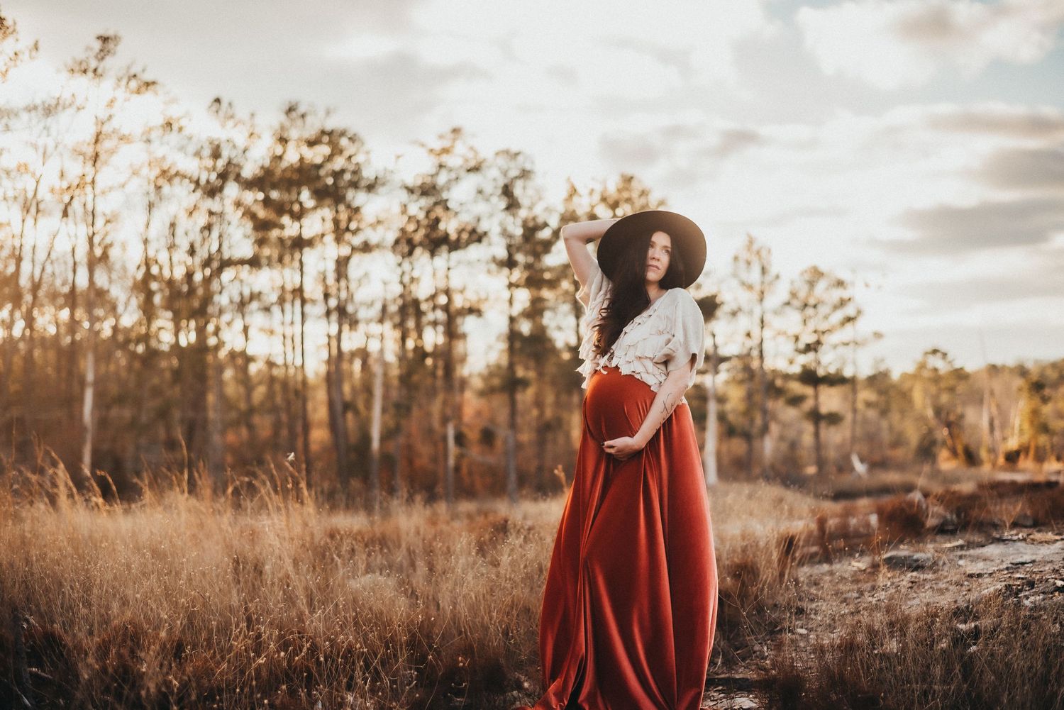 Expectant mother in flowing red skirt and white top posing in fall outdoor setting.