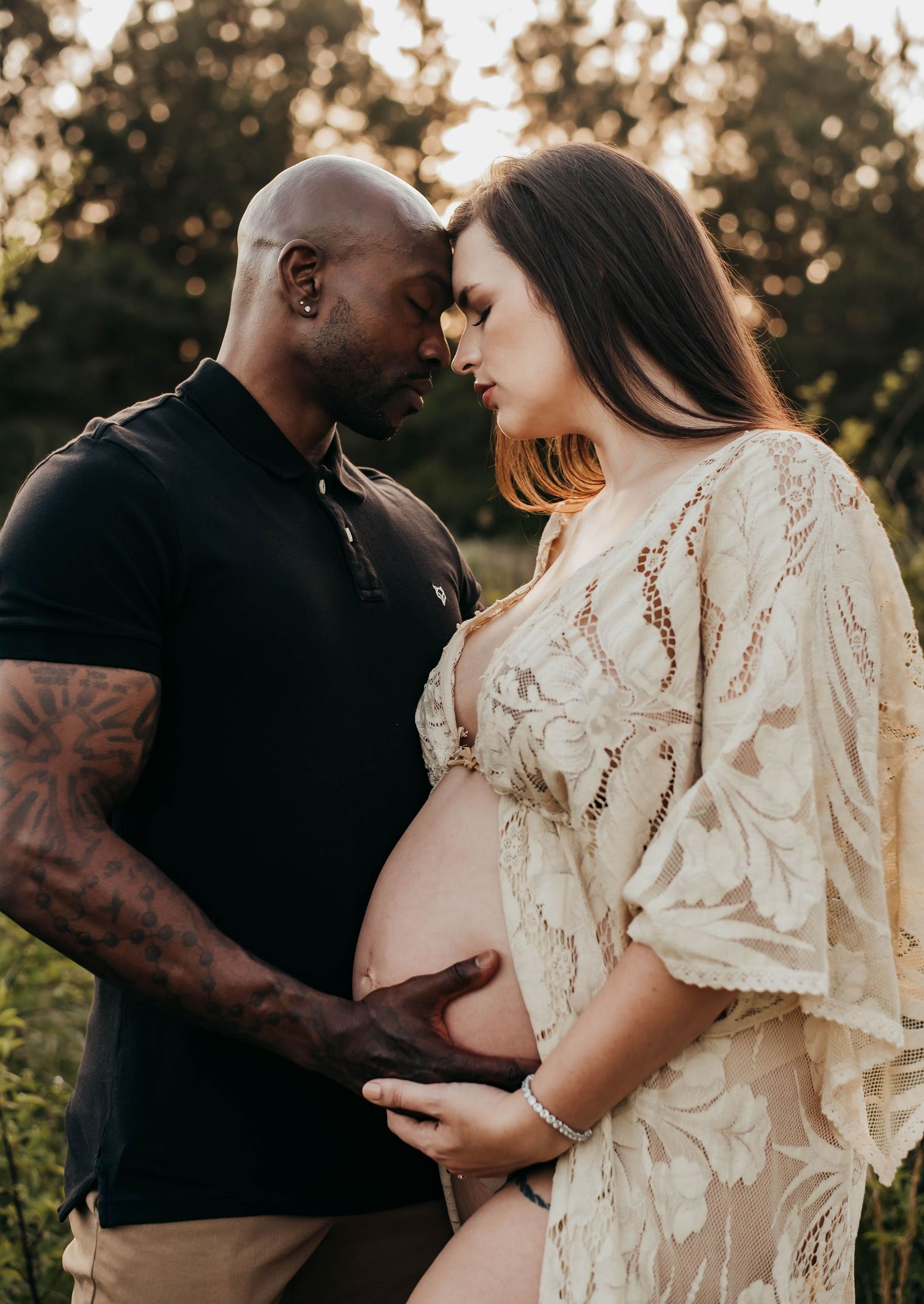 Couple sharing intimate maternity moment outdoors, man tenderly holding pregnant woman's belly at golden hour.