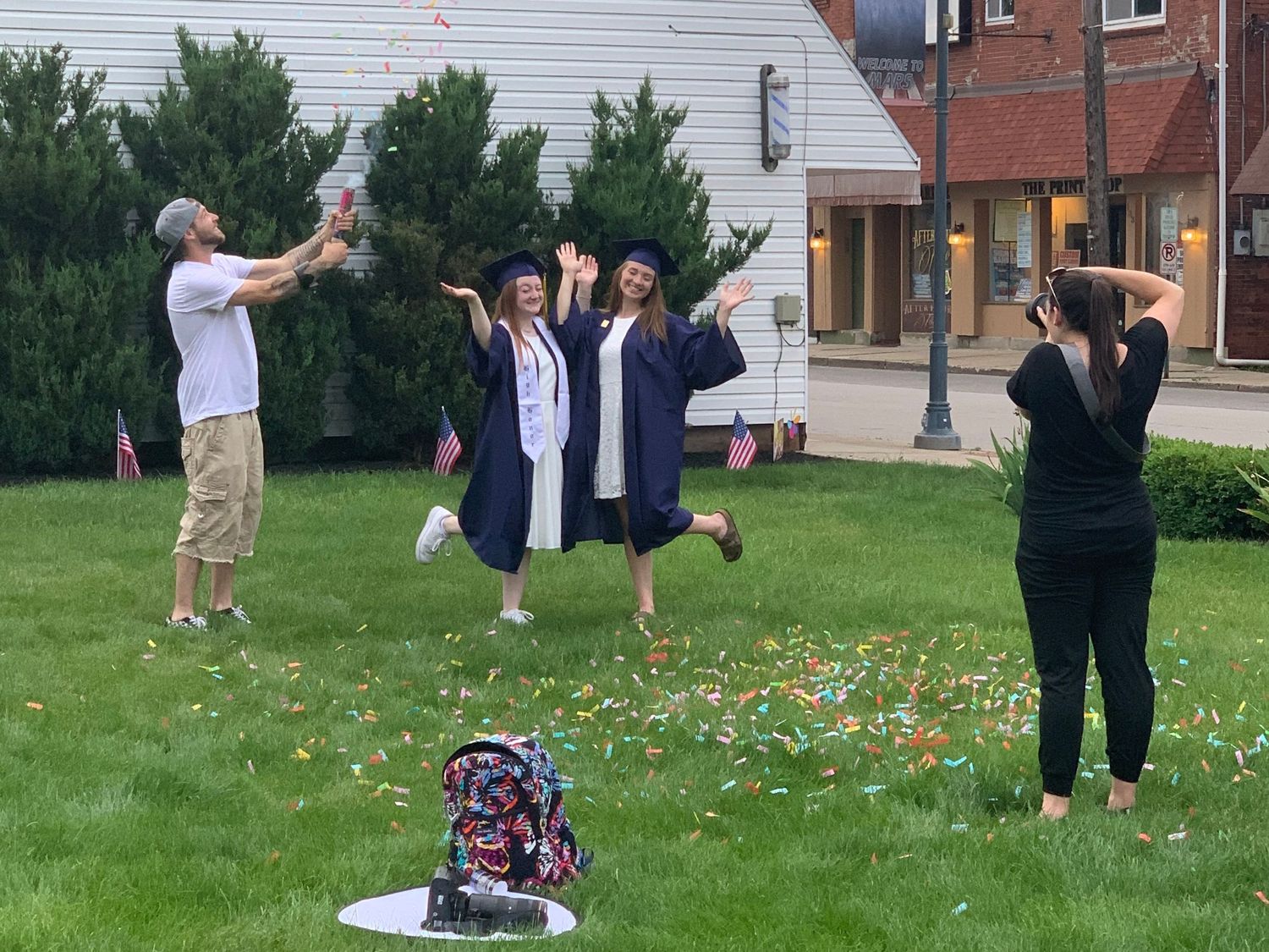A graduation celebration on a lawn with people jumping joyfully and posing for photos.