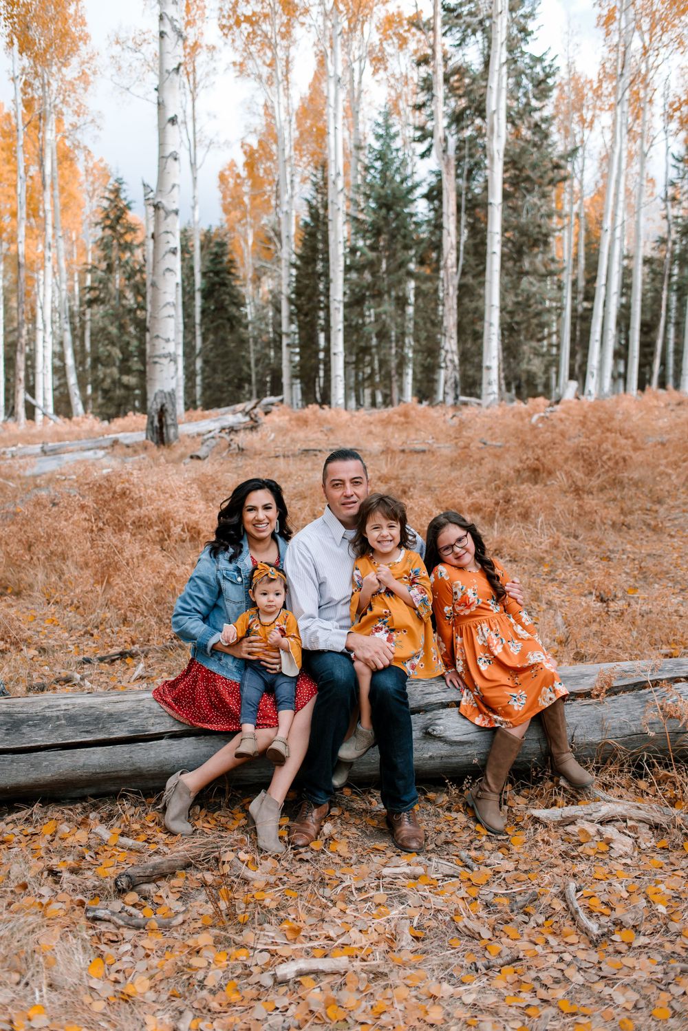A family sits together on a fallen log in an autumn aspen forest with orange and golden foliage.