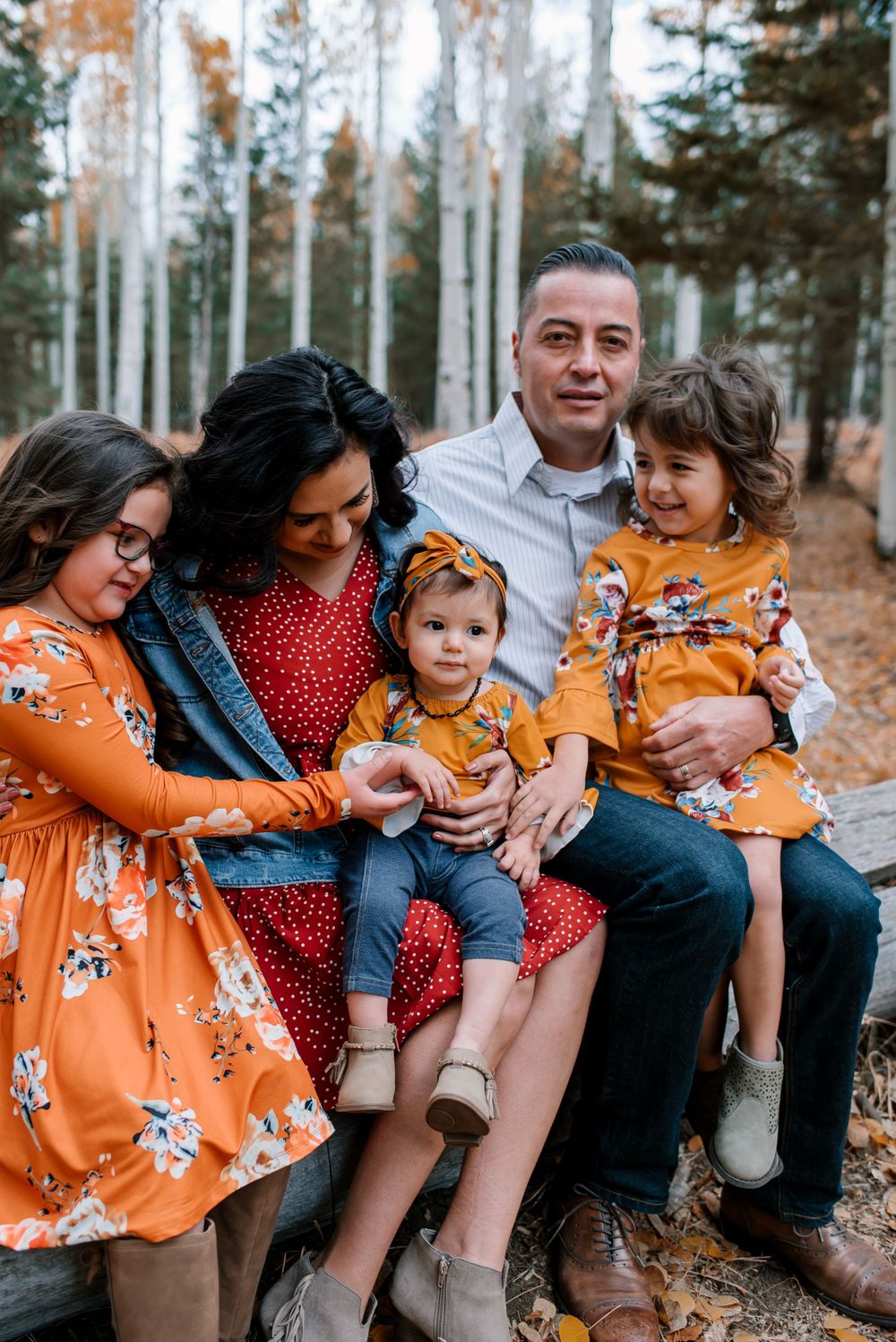 Family members share playful moments while sitting on a log surrounded by fall colors in an aspen grove.