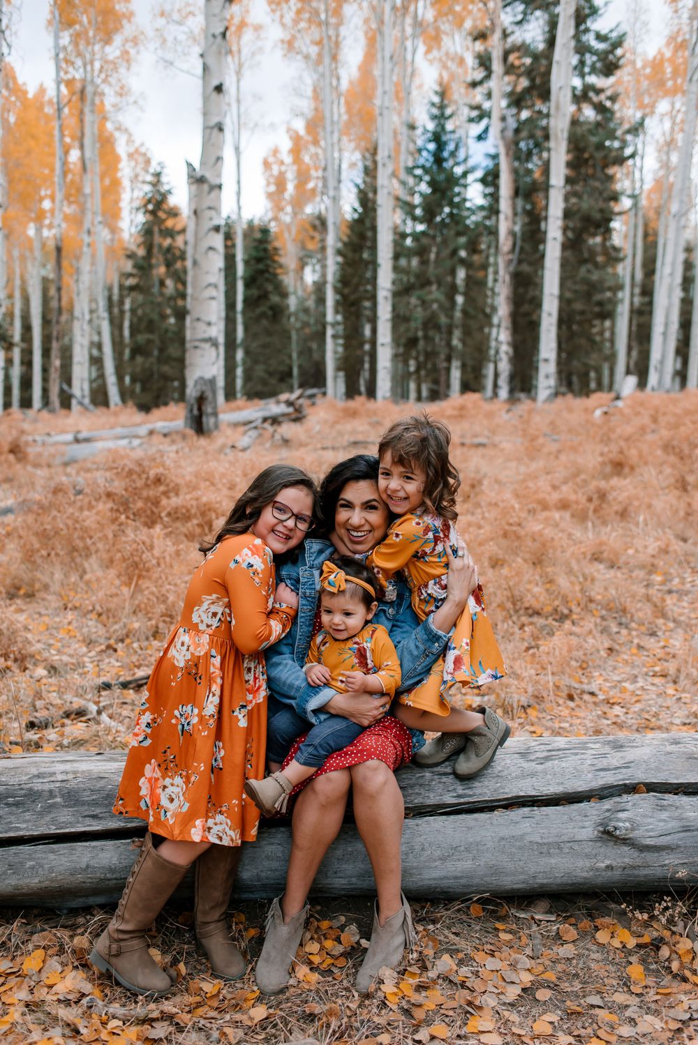 Family members cuddle together on a fallen log in a golden autumn forest setting.