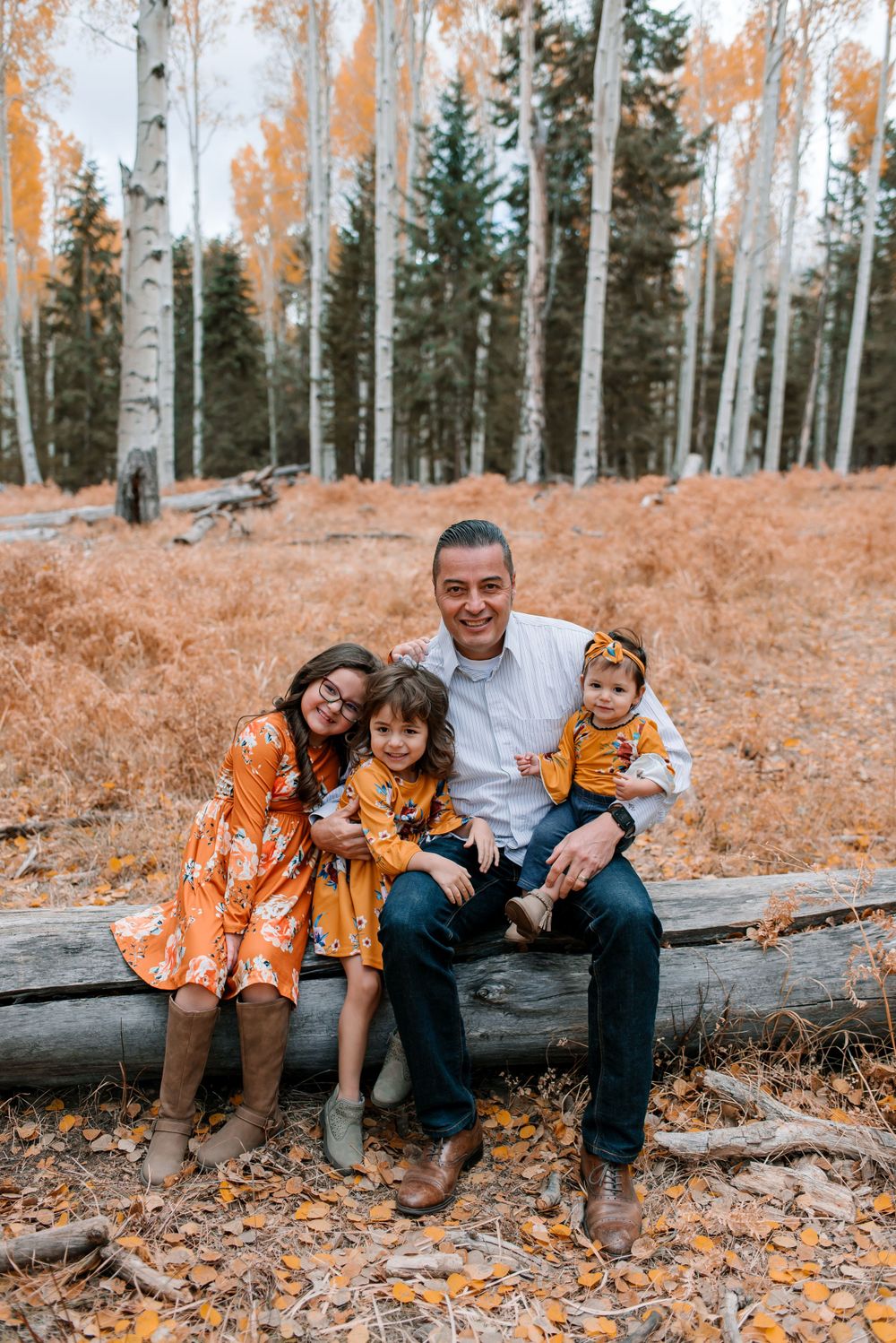 Family portrait on a fallen tree trunk surrounded by autumn aspens and fallen leaves.