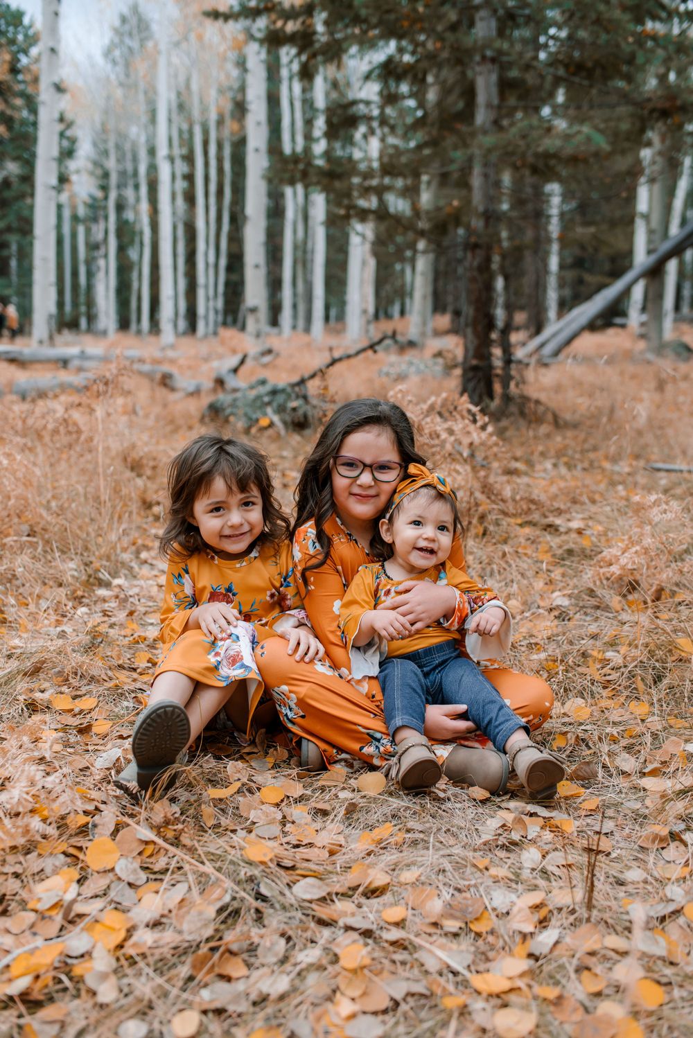 Children playing in fallen autumn leaves among white aspen trees.