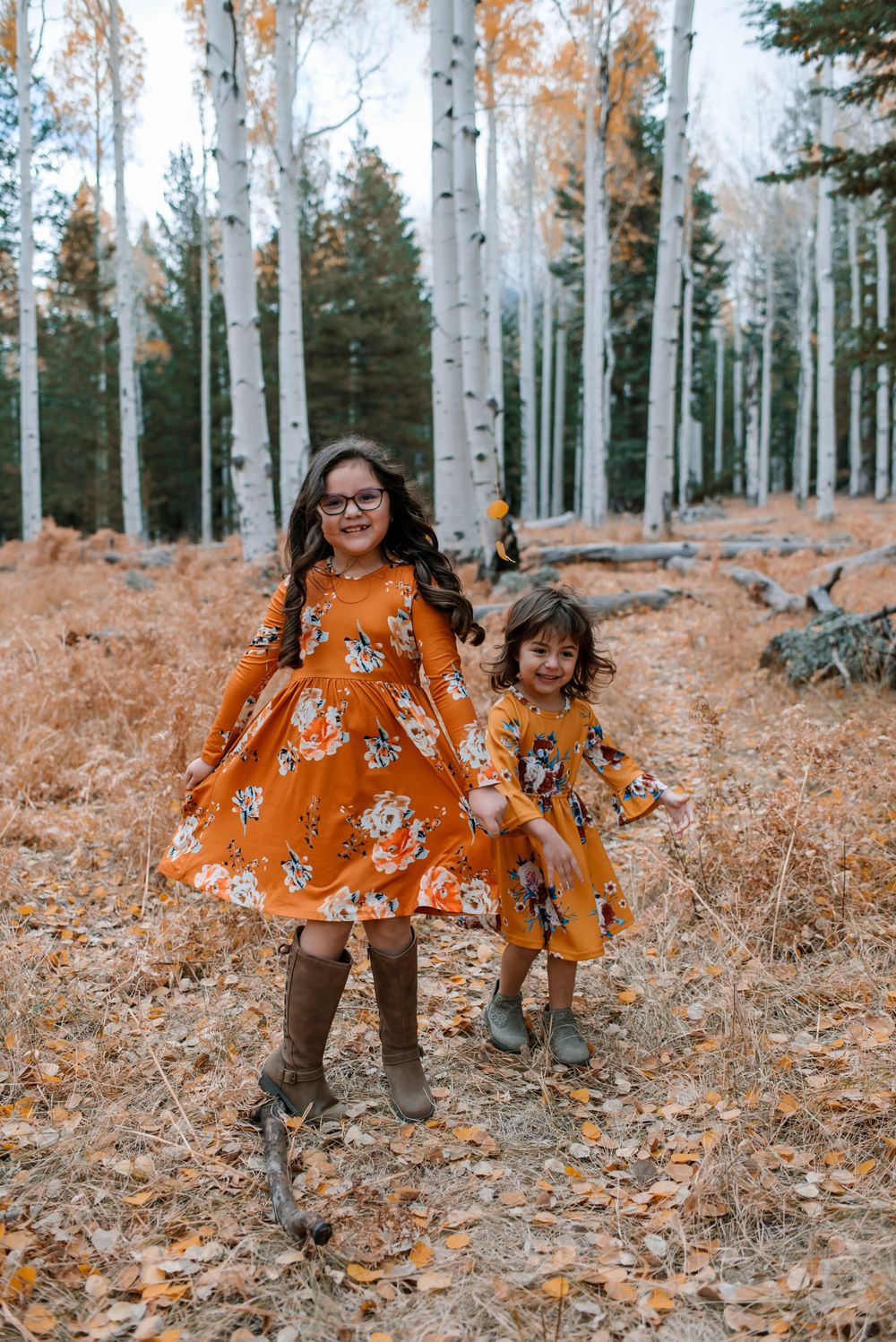 People in coordinating orange outfits explore a fall forest with white aspen trees.