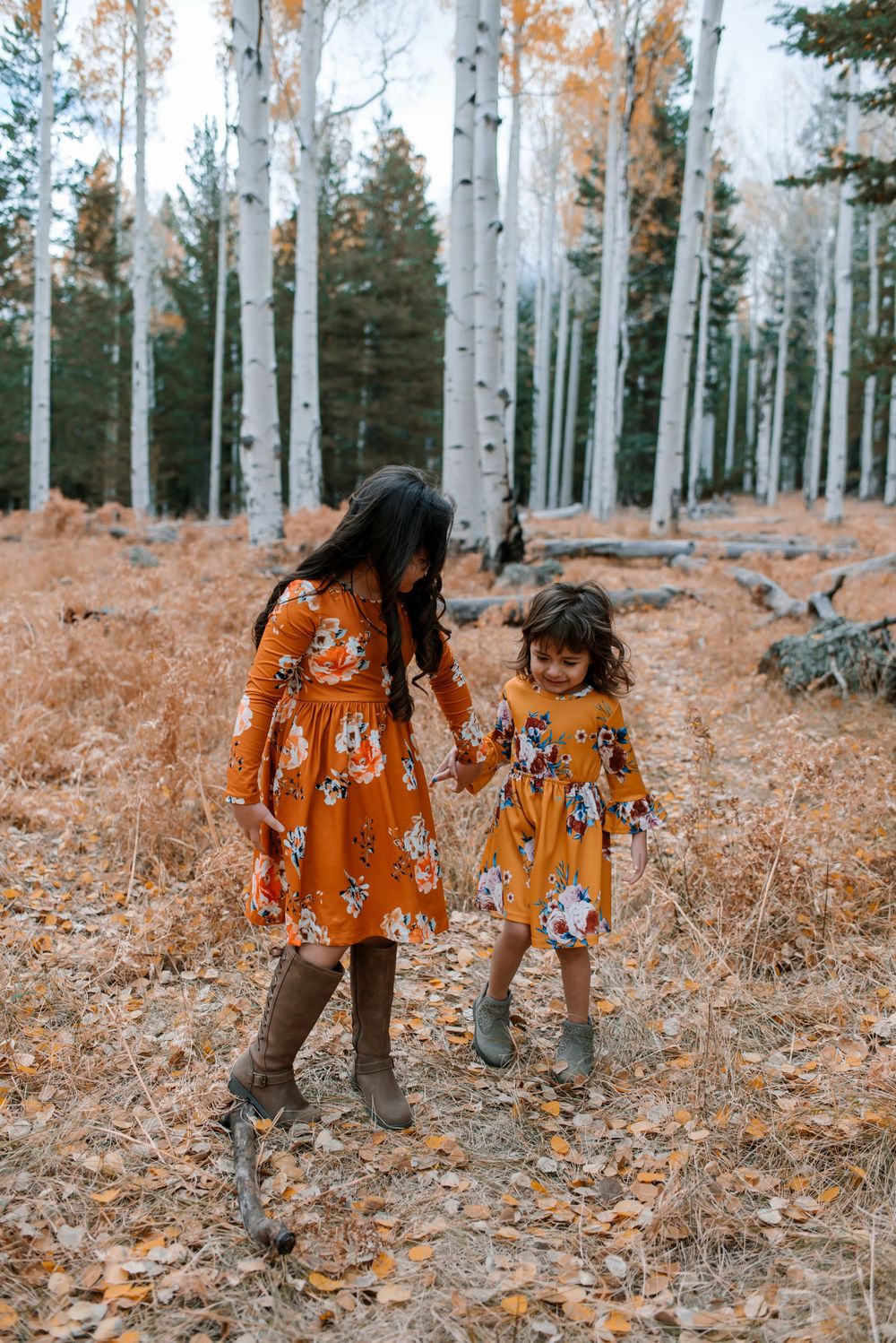 People in matching orange floral dresses walk through a golden aspen forest.