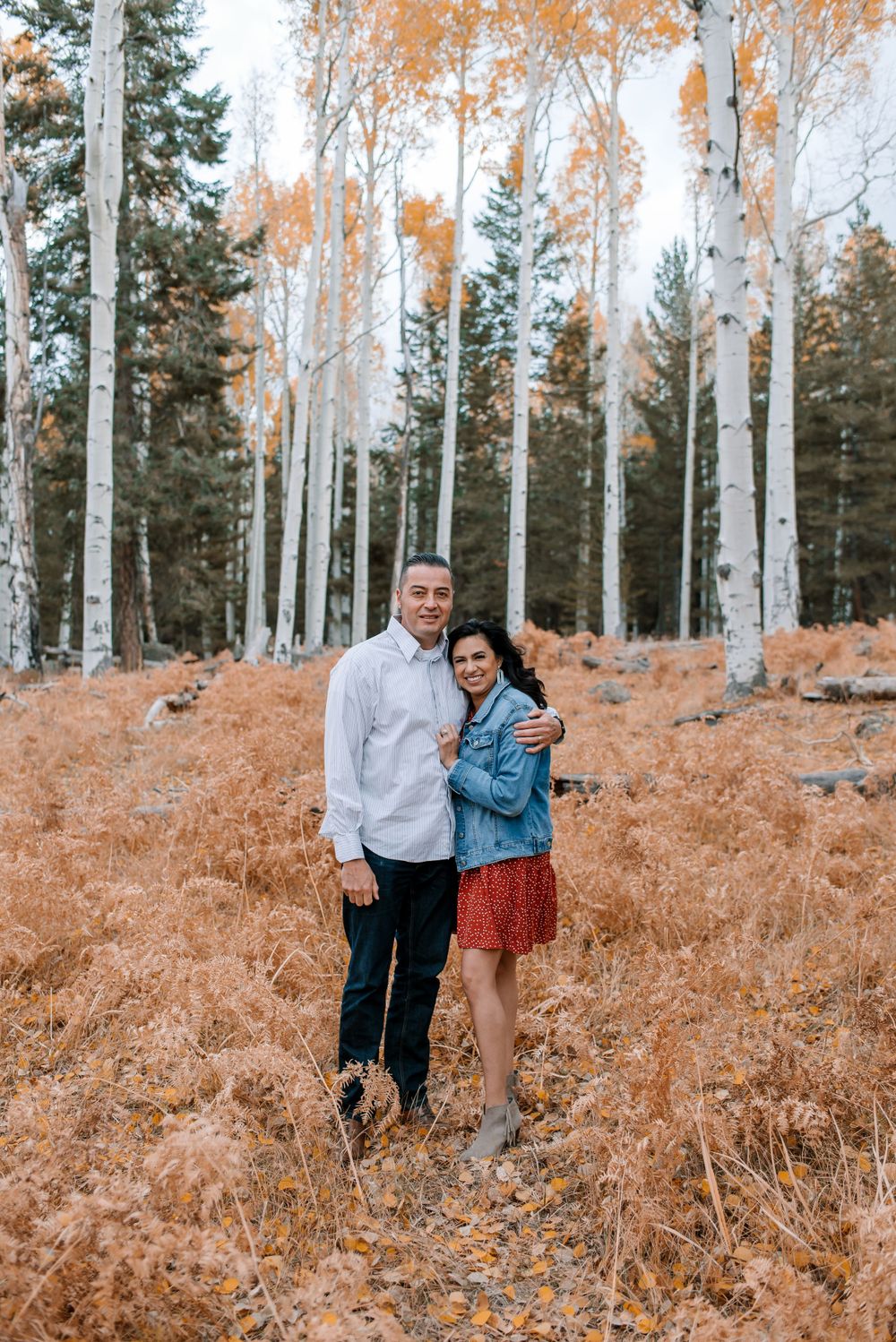 A couple poses together in a scenic aspen forest with golden autumn ferns creating a warm backdrop.