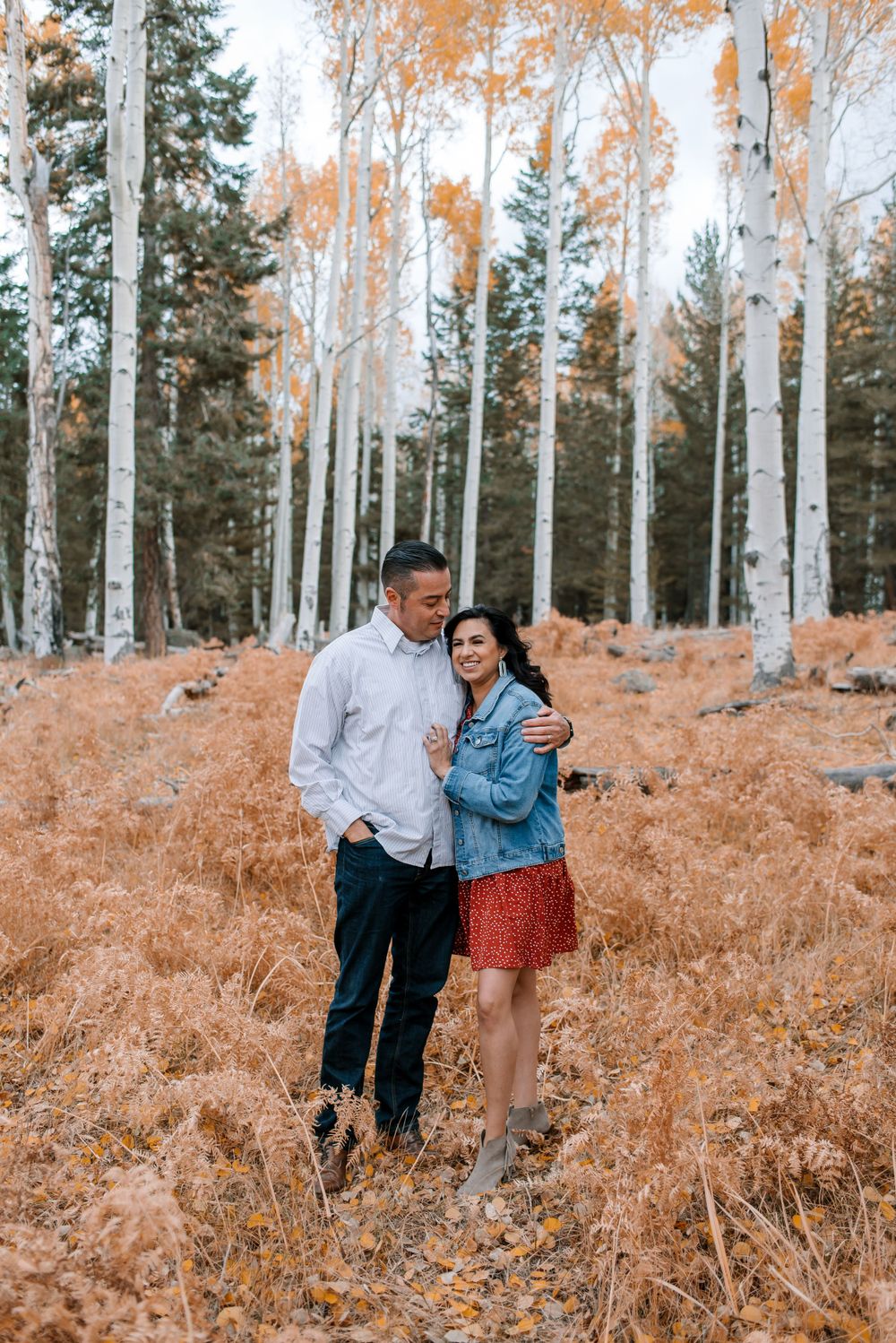 A couple embraces while standing among white aspen trees and orange fall foliage.