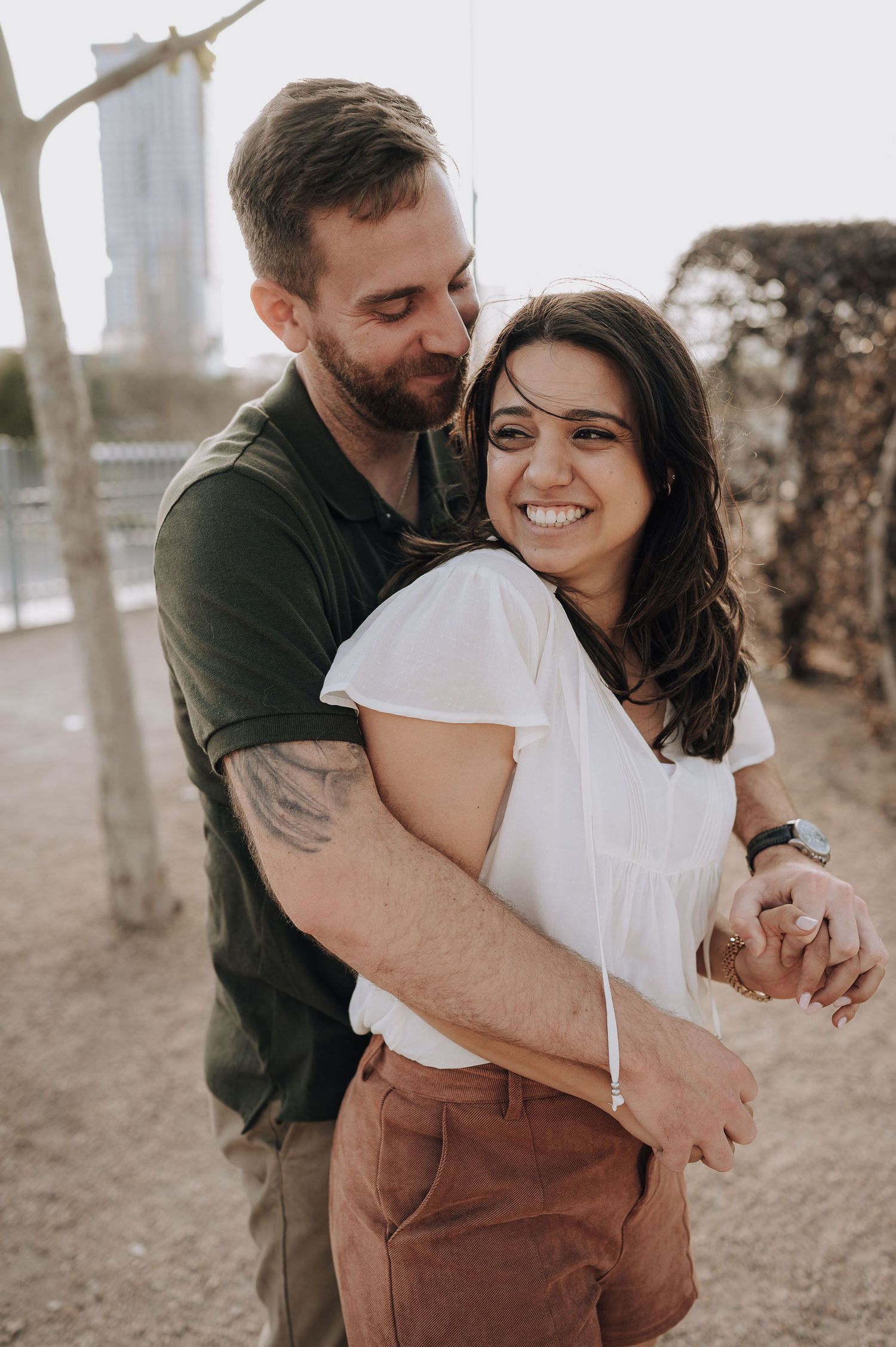 A romantic couple embracing outdoors in a candid moment with a white building visible in the background.
