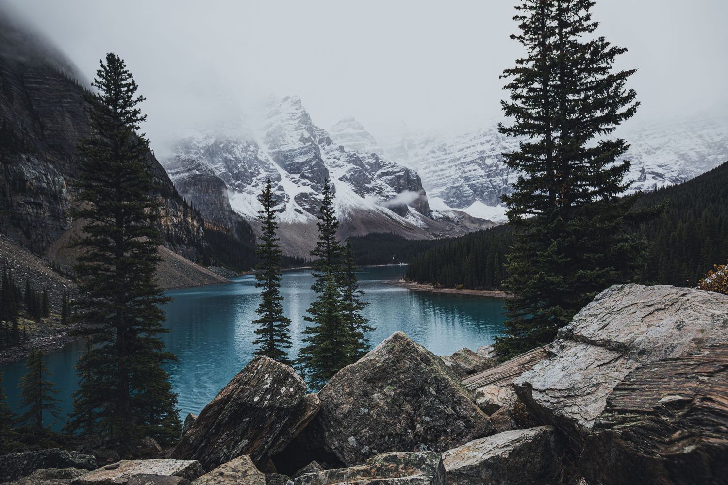 Snow-capped mountains reflect in the turquoise waters of Moraine Lake surrounded by evergreen forest.