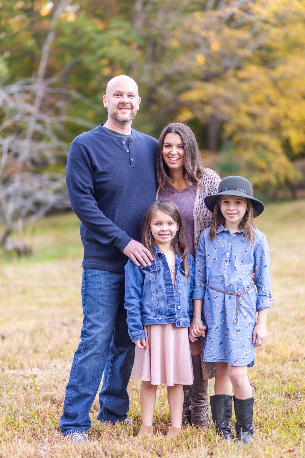 Family of four in coordinating blue outfits posing outdoors in autumn setting.