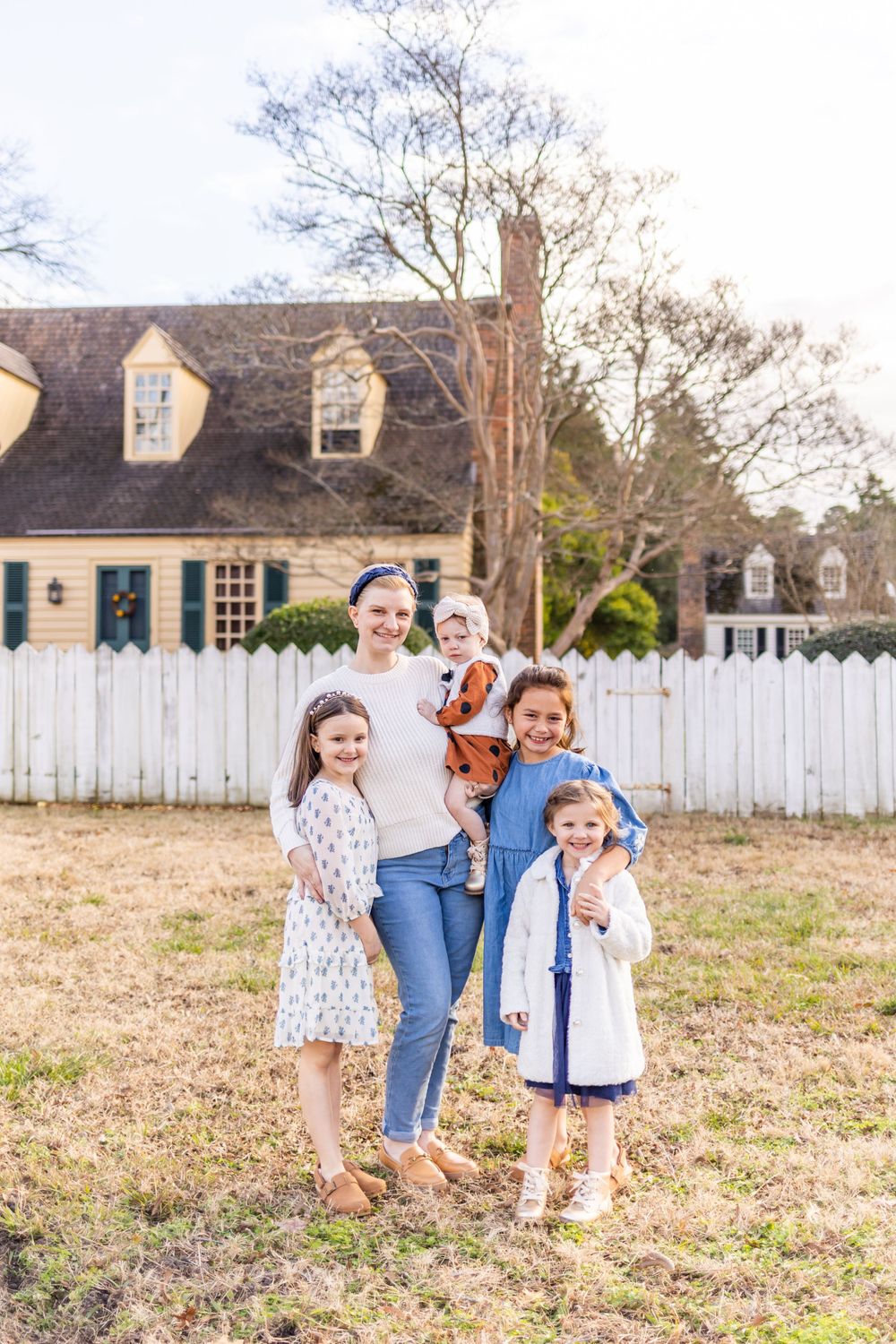 Group portrait in front of historic white colonial house with black shutters and picket fence.