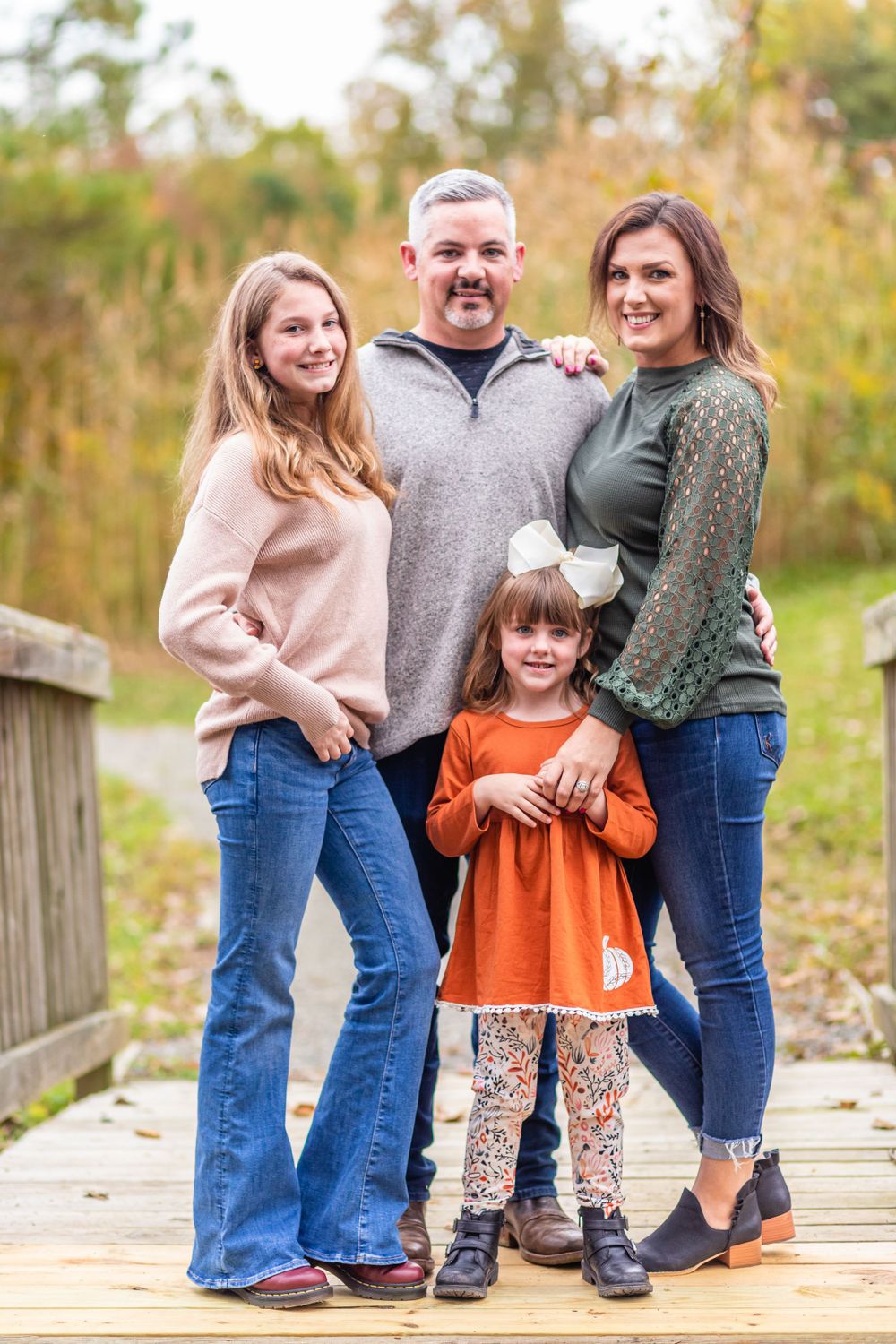 Casual family portrait on wooden bridge during fall season.