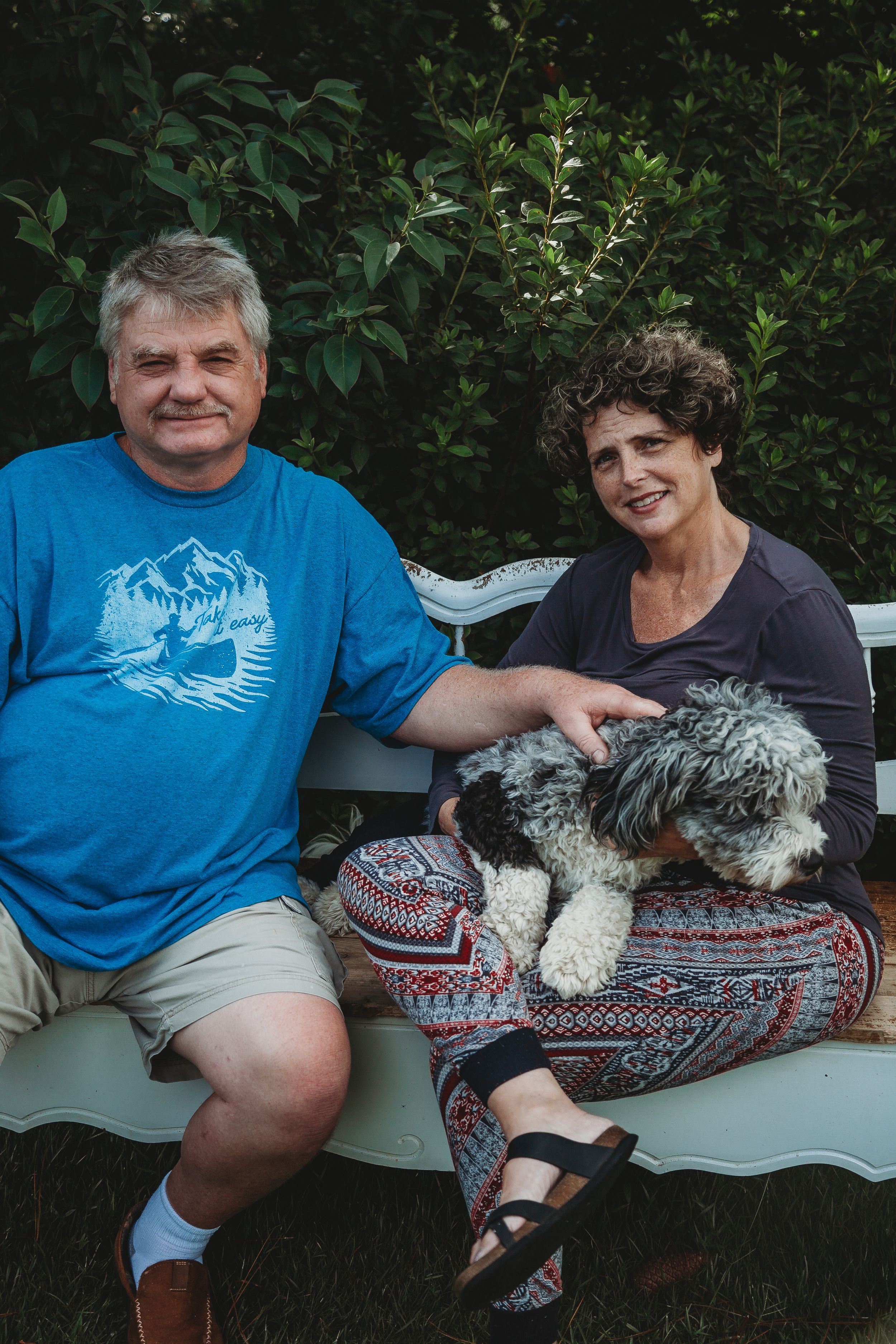 Family members sitting together with their dog on a white bench in an outdoor garden setting.