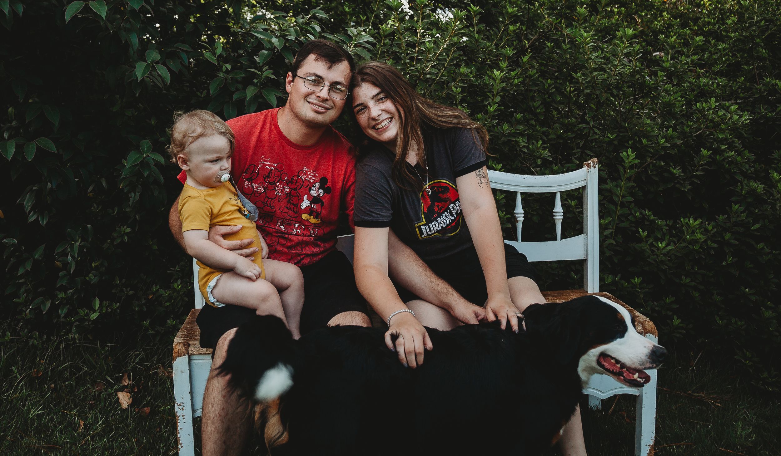 Family members gathered on an outdoor bench with their pets for a casual photo.