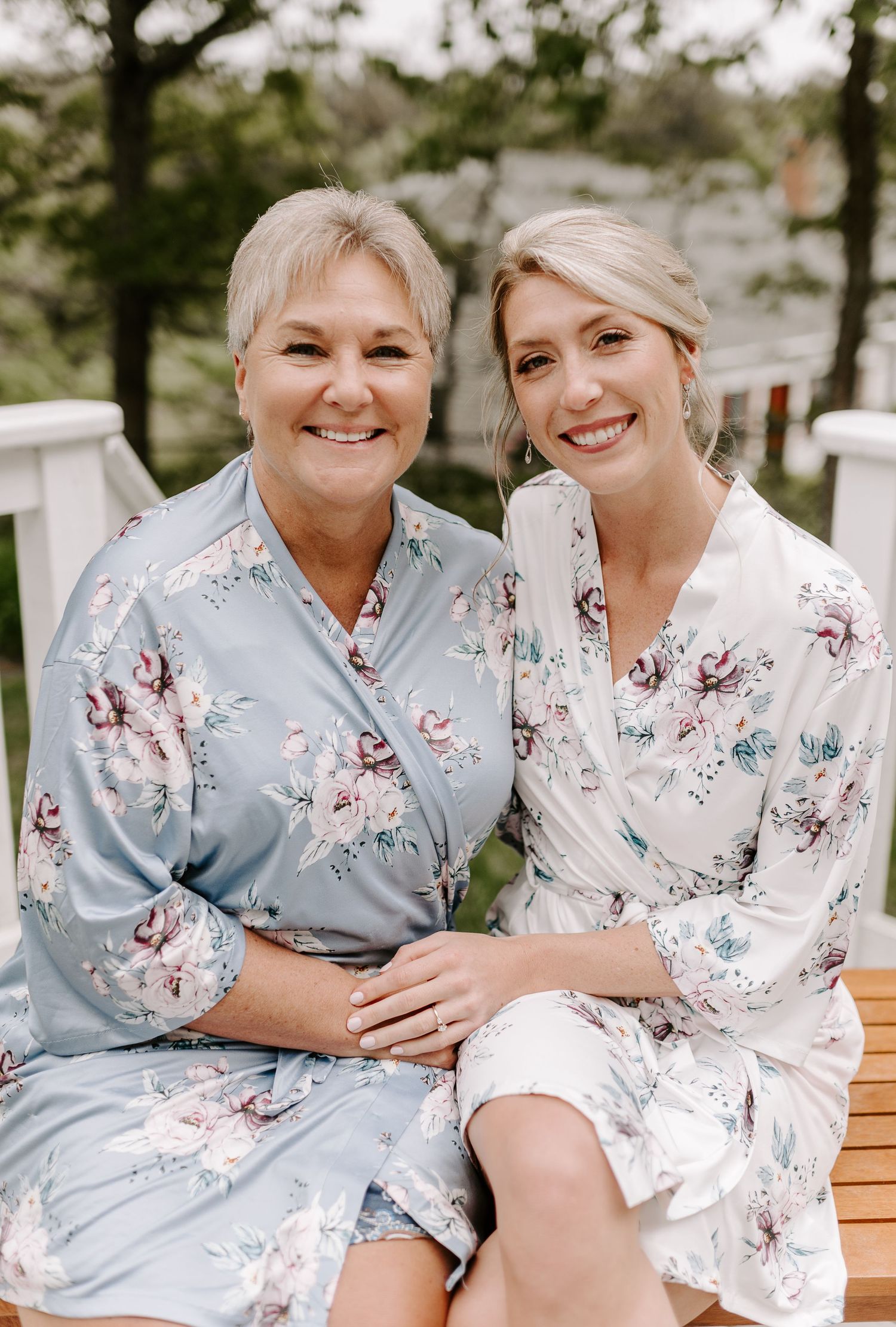 Two people in floral robes sit close together on a wooden bench outdoors.