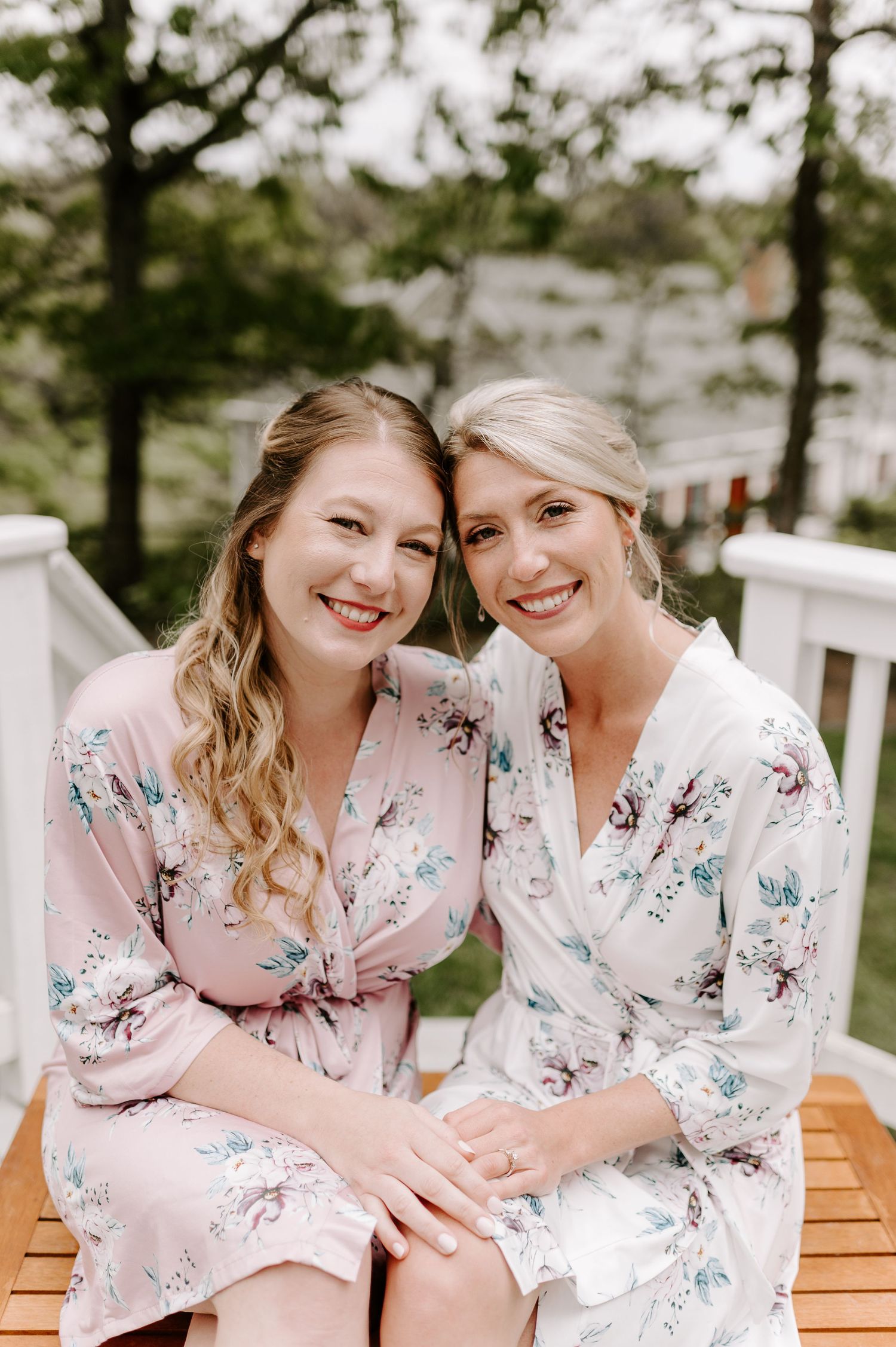 Two people in pink and white floral robes share joyful laughter on a wooden bench.