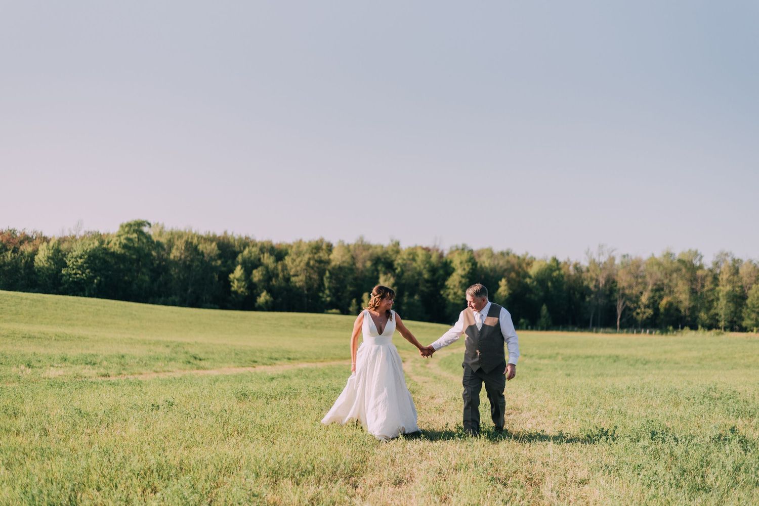 Couple walking in field holding hands at country wedding