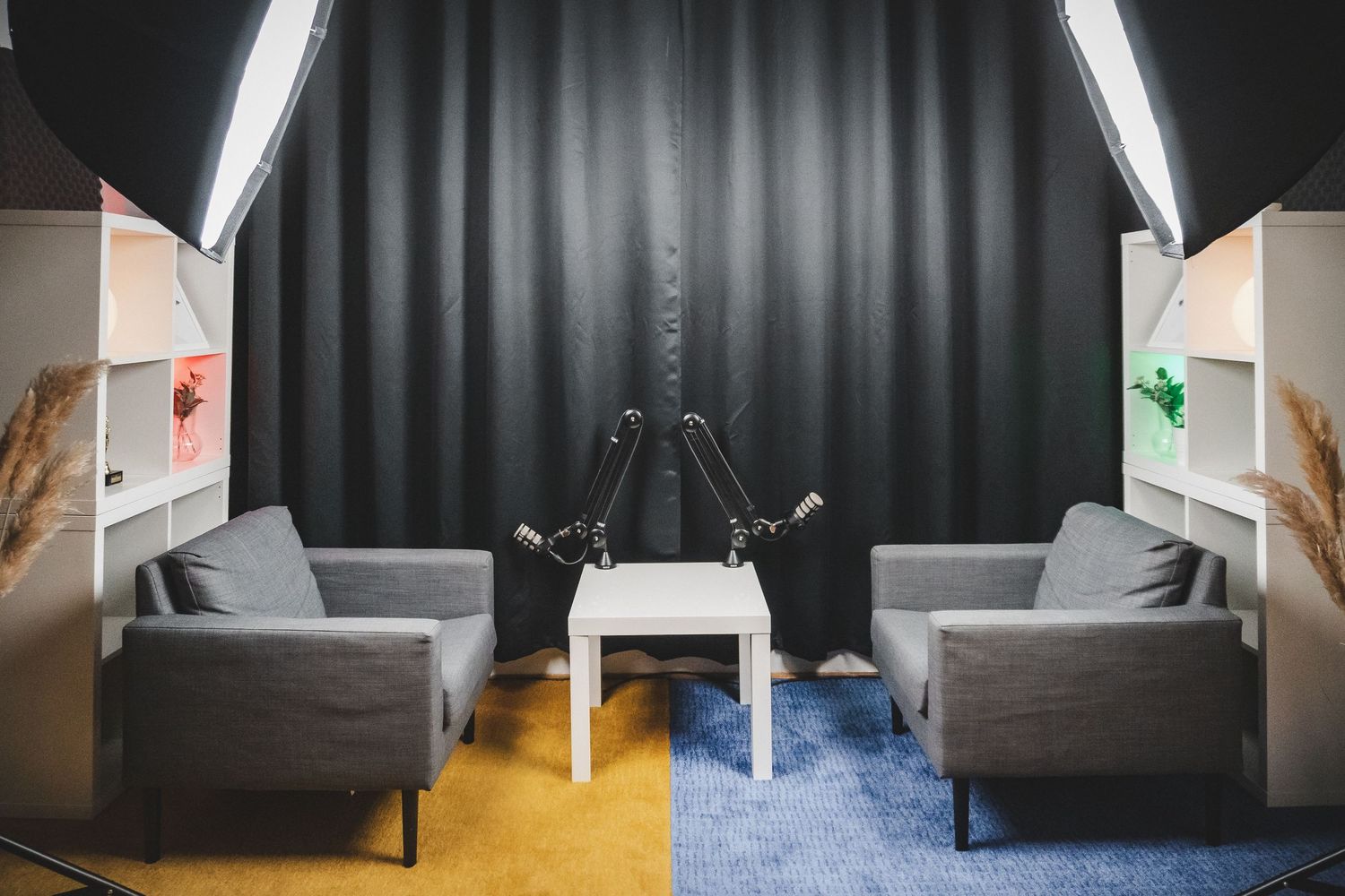 Modern podcast recording studio setup with two gray armchairs and studio lighting equipment.