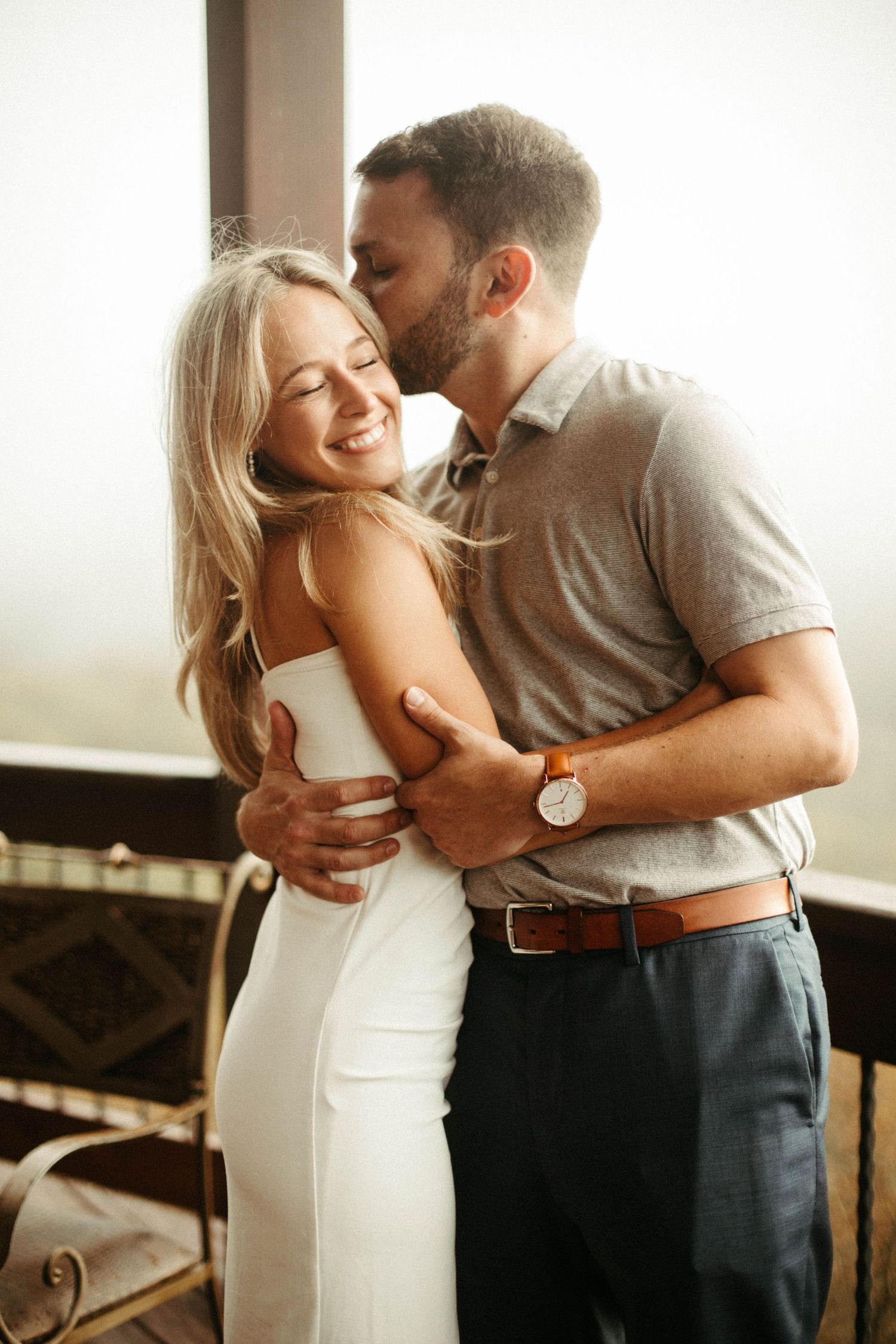 Romantic couple embracing in soft window light during an intimate photoshoot.