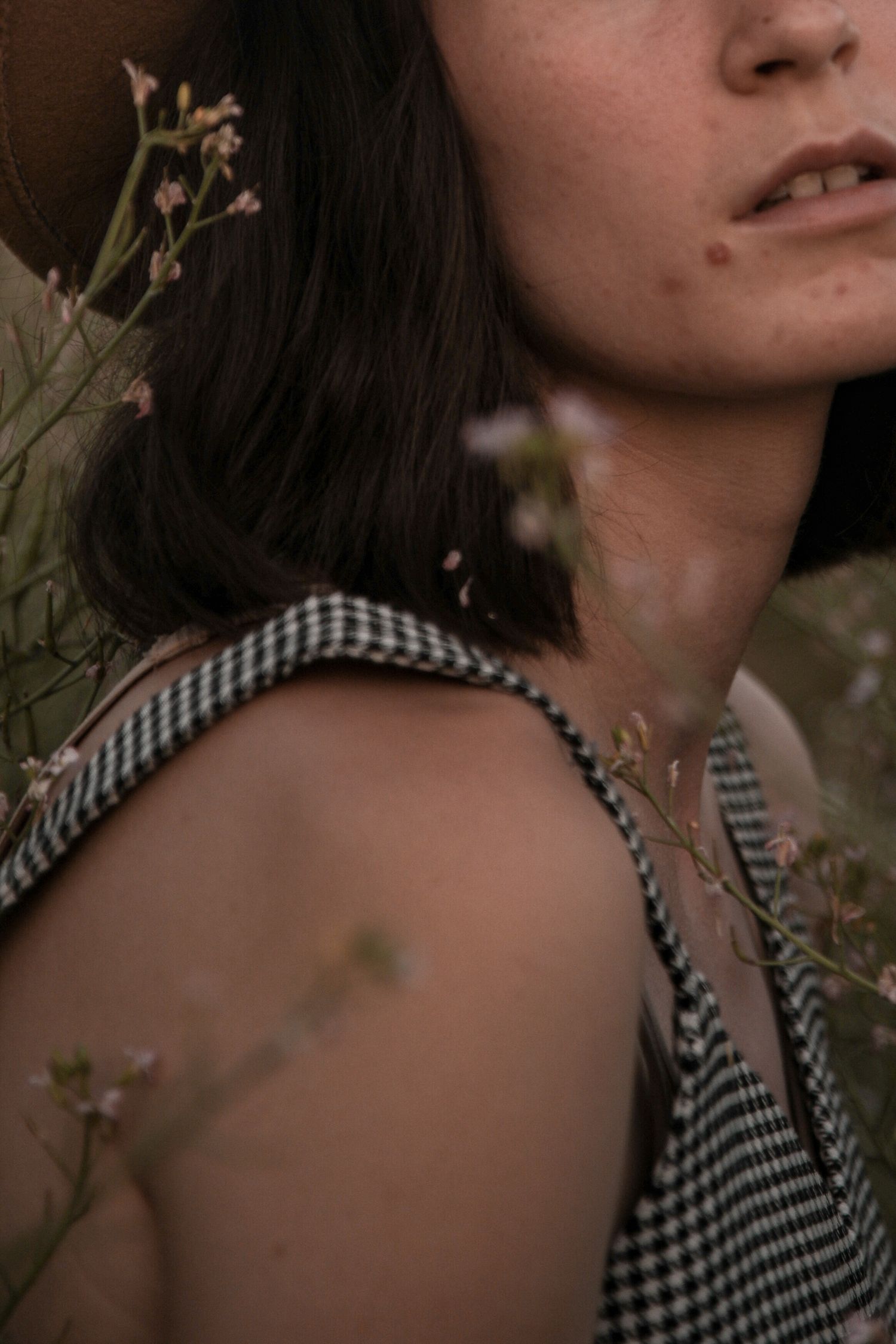 Close-up portrait showing gingham dress strap and wildflowers in soft evening light.