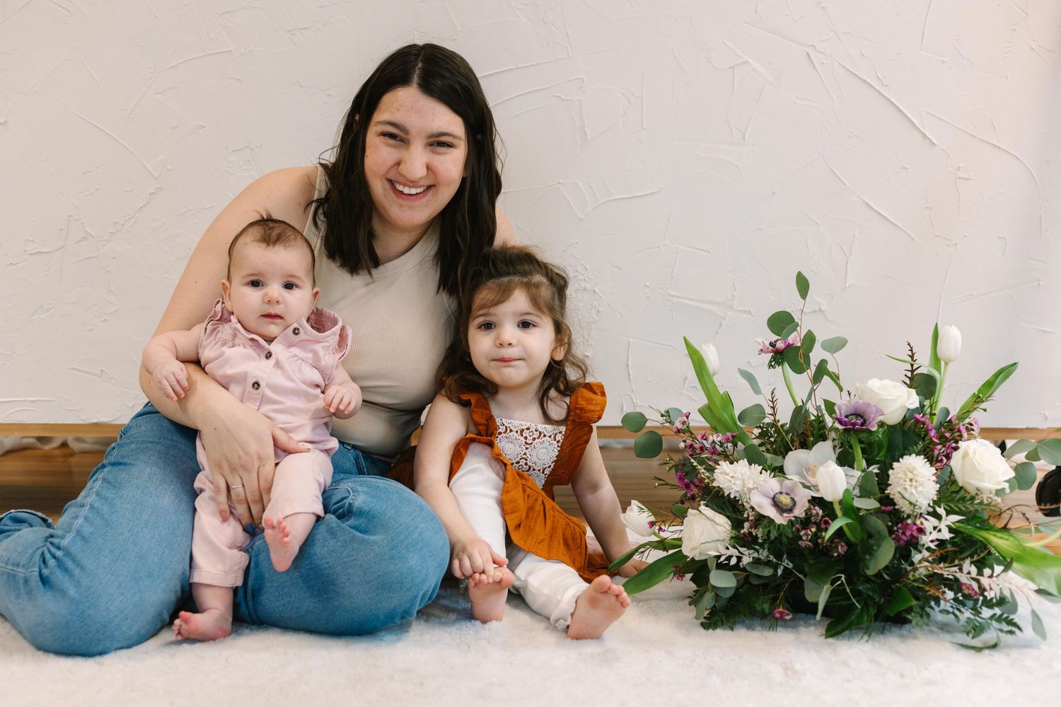Indoor portrait with floral arrangement showing individuals sitting near pink and white flowers.