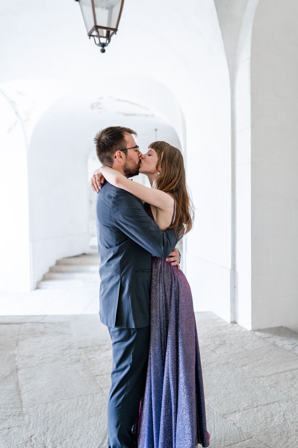 Romantic embrace under arched white corridor with hanging lantern above.