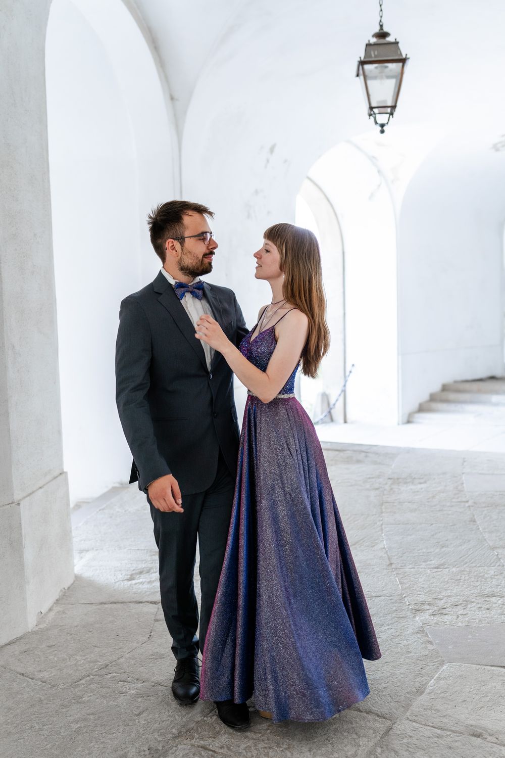 Romantic moment between couple in formal wear under arched white corridor.