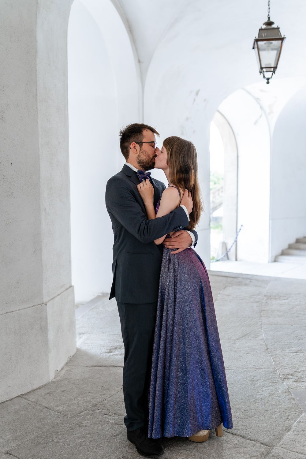 Intimate moment between couple in formal wear under white archways.