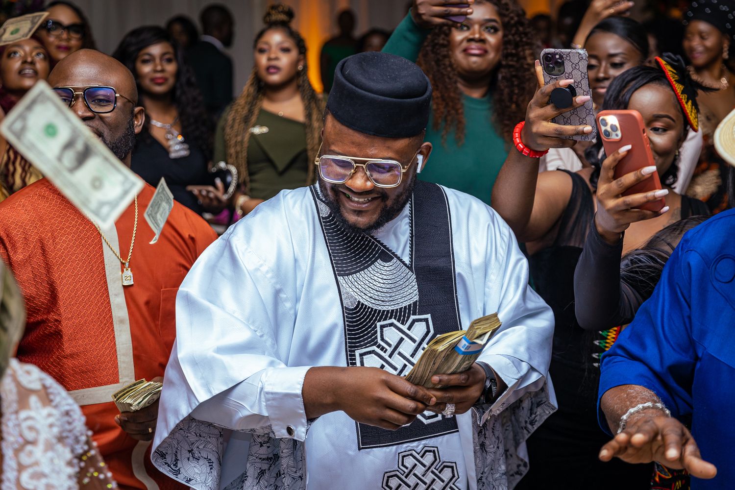 Man in traditional attire holding money surrounded by a crowd at an event.
